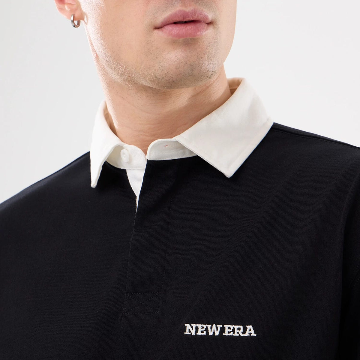 New Era Black Short Sleeve Rugby Shirt, close-up on a model showing the contrasting white collar and embroidered NEW ERA logo on the right chest, with the top button undone for a casual look.