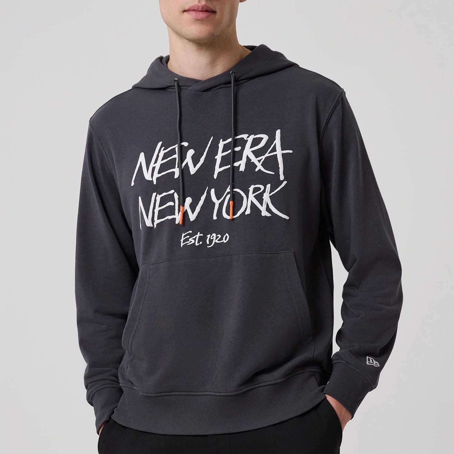 New Era New York Dark Grey Oversized Pullover Hoodie, front view showing the large white graphic text "New Era New York" with "Est. 1920" below on the dark grey fabric, and a debossed New Era logo on the left sleeve near the cuff.