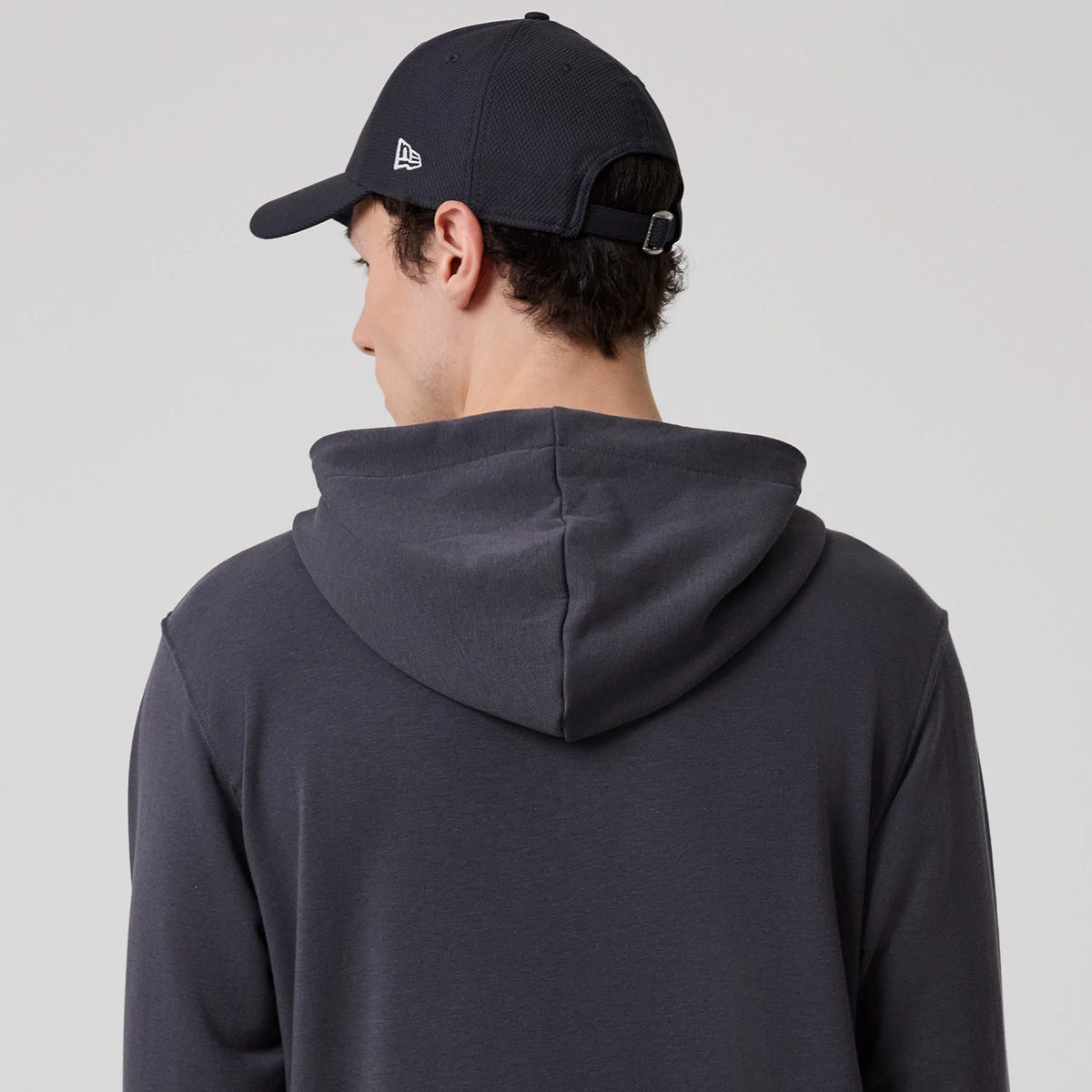 New Era New York Dark Grey Oversized Pullover Hoodie, rear view showing the hood draped over the back, worn by a person wearing a dark cap with a white raised New Era logo on the side.