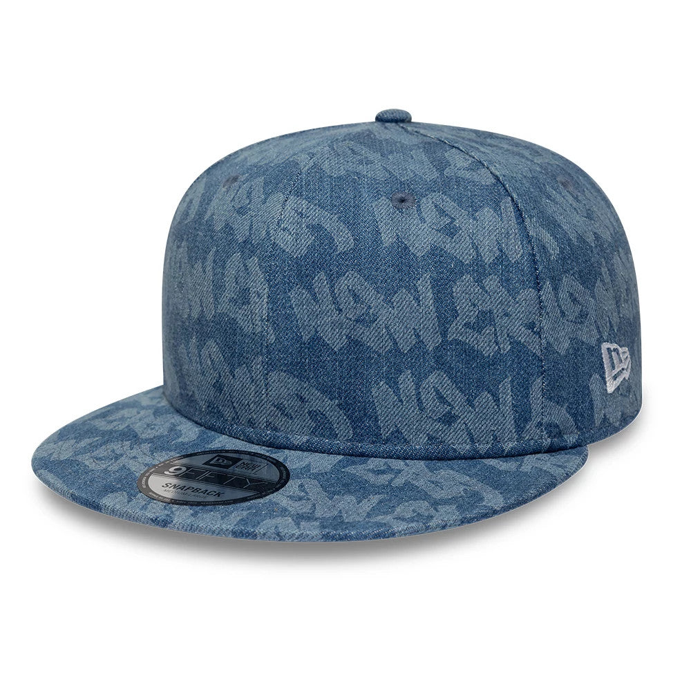 New Era Laser Burnout Washed Denim Navy New Era 9FIFTY Snapback Adjustable Cap, three-quarter view showing the all-over graffiti pattern in washed denim, flat visor with 9FIFTY size sticker, and white New Era flag logo on the left side.