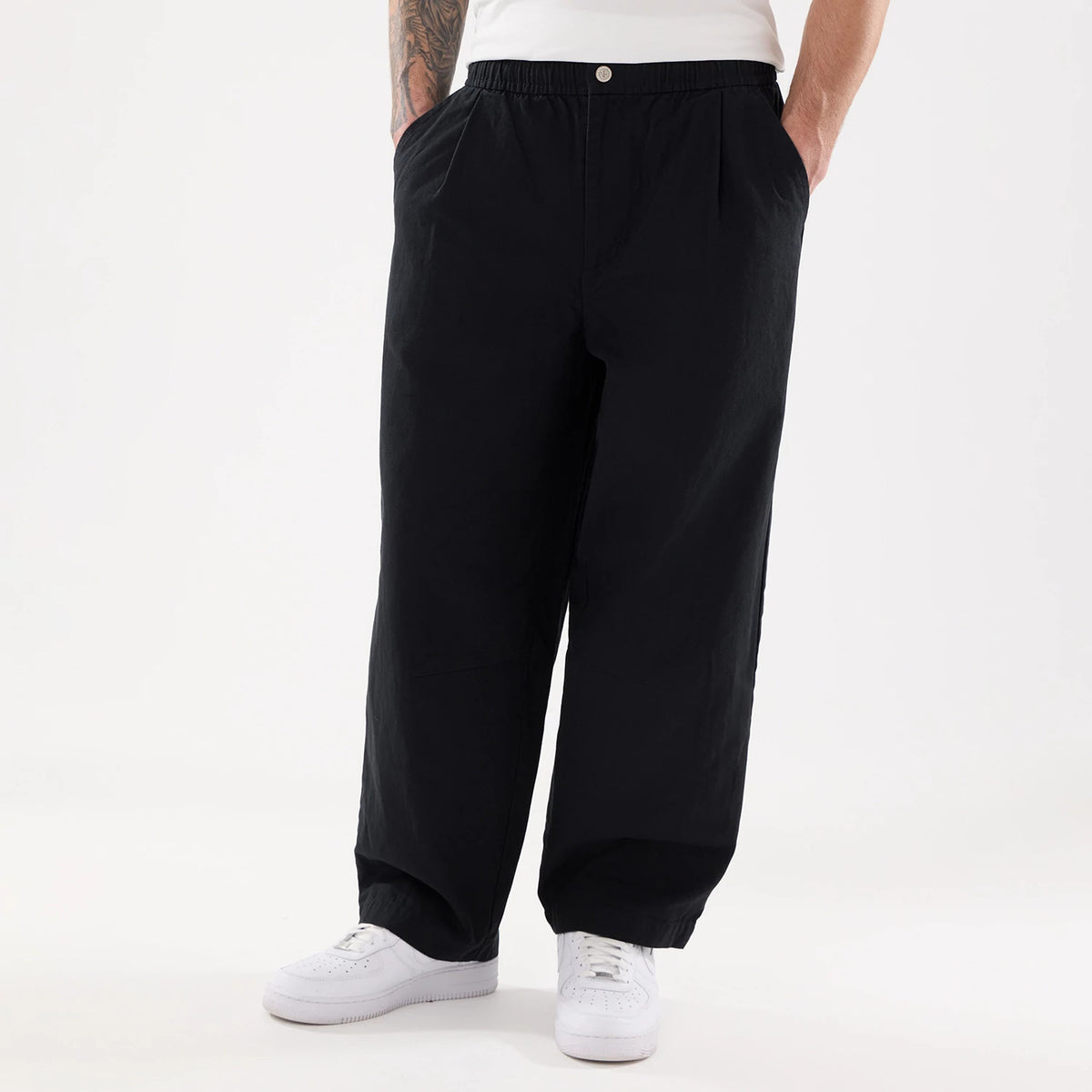 New Era Black Balloon Leg Trousers, front view on a model showcasing the relaxed balloon leg fit and an elasticated waistband with side pockets, styled with a white T-shirt and white sneakers.