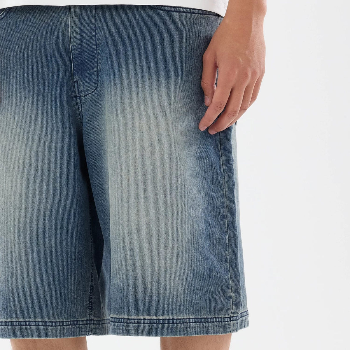New Era Washed Blue Bermuda Shorts, front view showing the faded blue denim fabric with a loose fit, visible stitching along the seams, and a plain waistband accentuating the relaxed design.