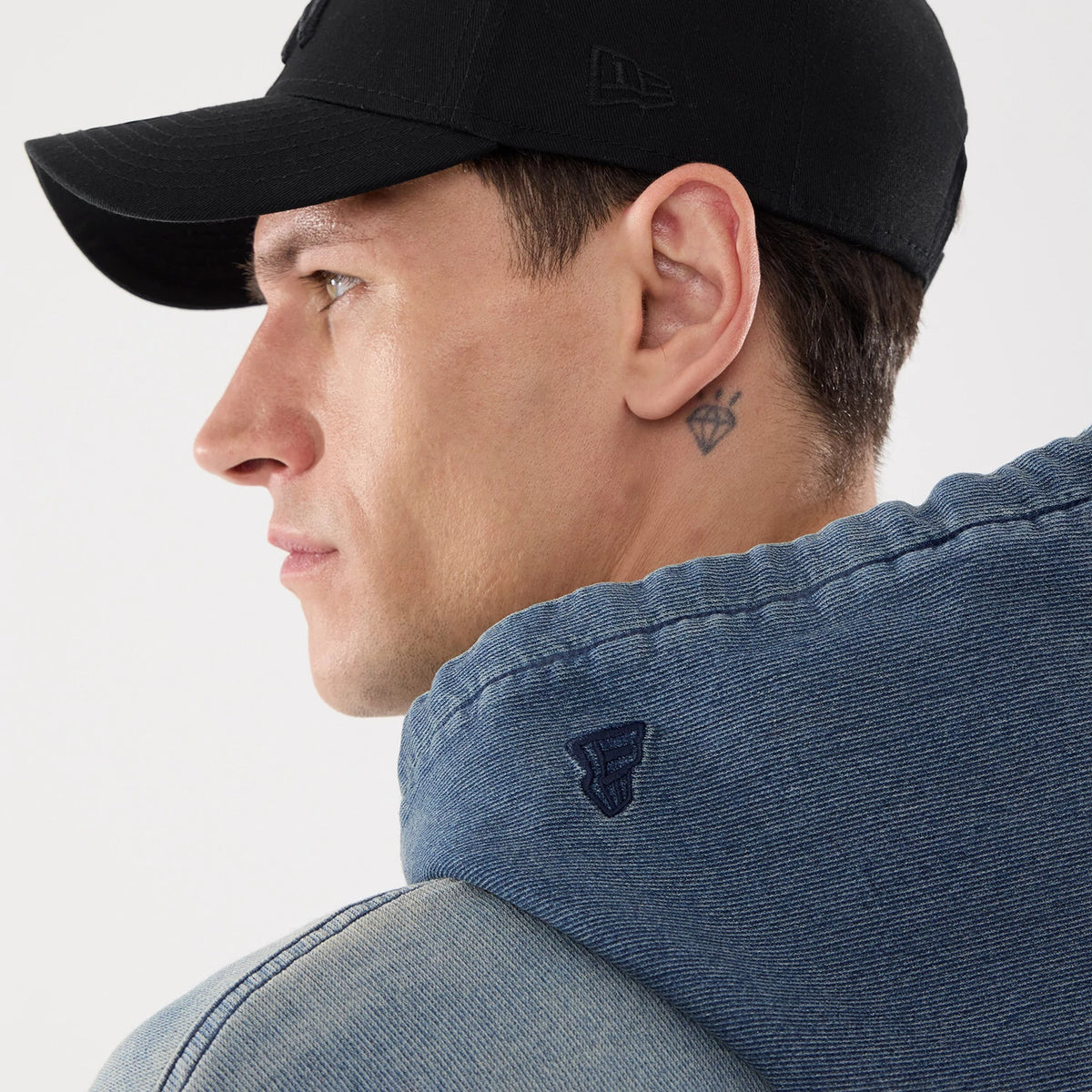 New Era Washed Blue Full Zip Hoodie, on-model view showing the back of the washed blue hoodie with a raised New Era logo on the side of the hood, worn with a black cap featuring a raised New Era logo on the side.