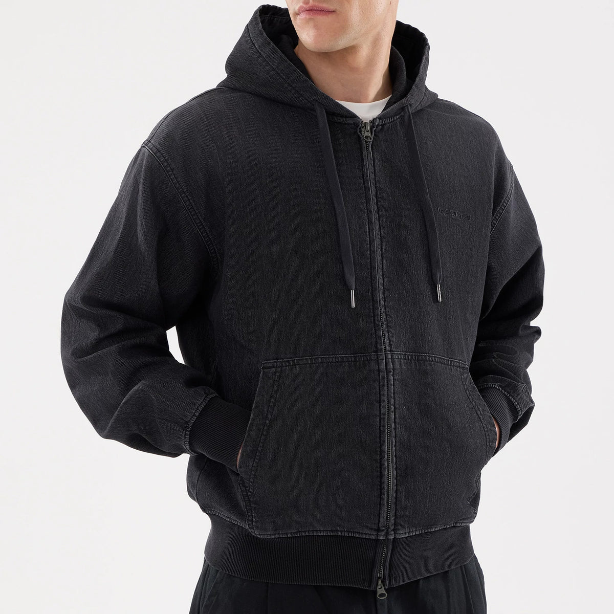 New Era Washed Black Full Zip Hoodie, on-model view showing the washed black hoodie with a full zip closure, drawstring hood, ribbed cuffs and hem, a front pouch pocket, and a debossed New Era logo on the chest.