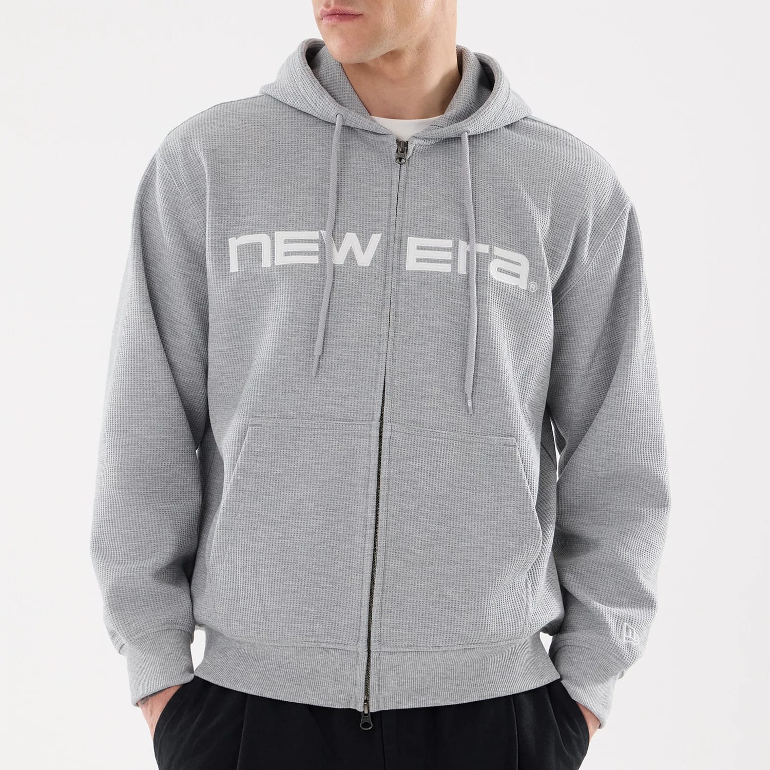New Era Waffle Grey Full Zip Hoodie, front view showing the grey fabric with a white embossed New Era logo across the chest, a full-length zip down the centre, drawstring hood and a small logo on the left wrist.