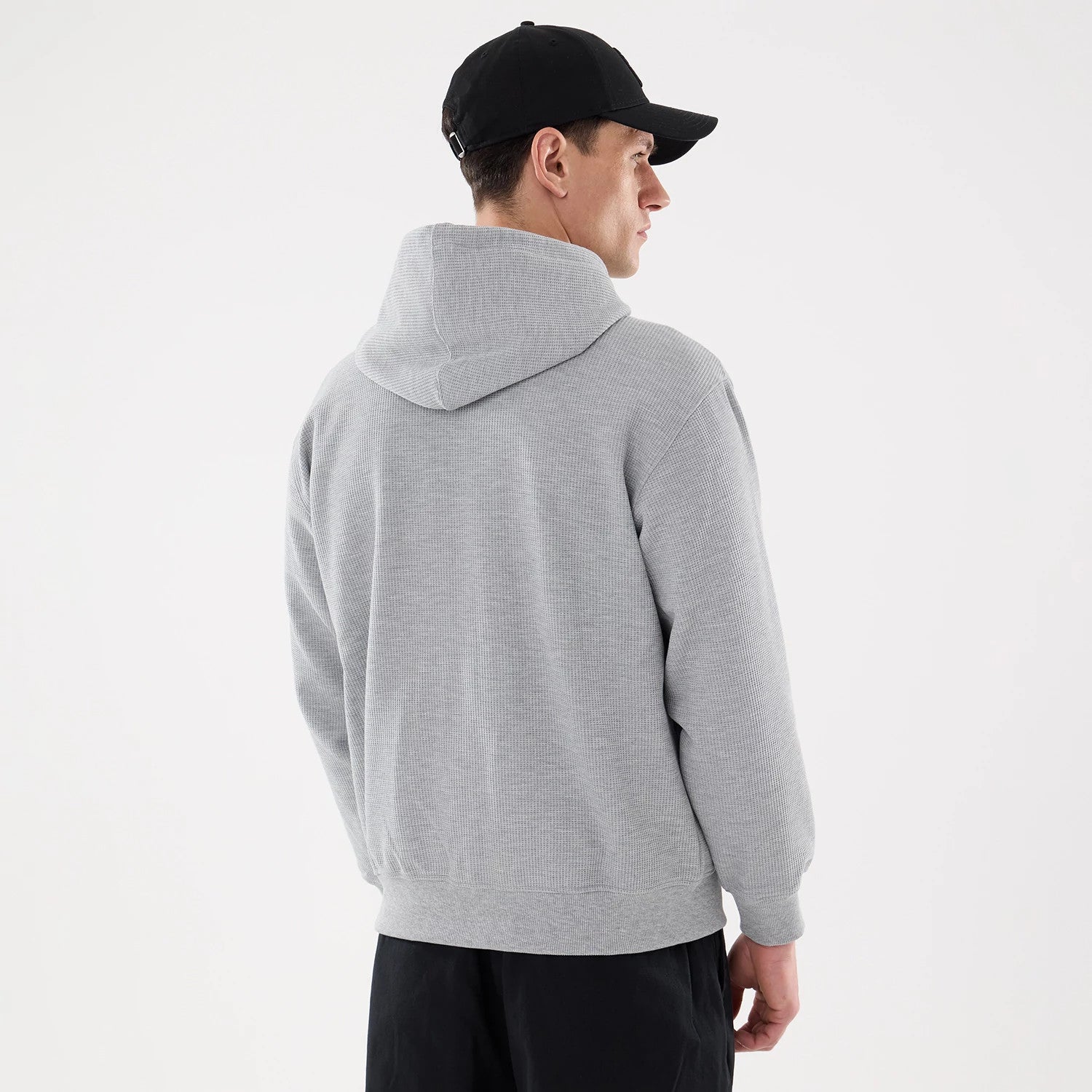 New Era Waffle Grey Full Zip Hoodie, rear view showing the light grey textured hoodie with the hood up, covering the upper back, and long sleeves falling naturally to the wrists on a model wearing a black cap.