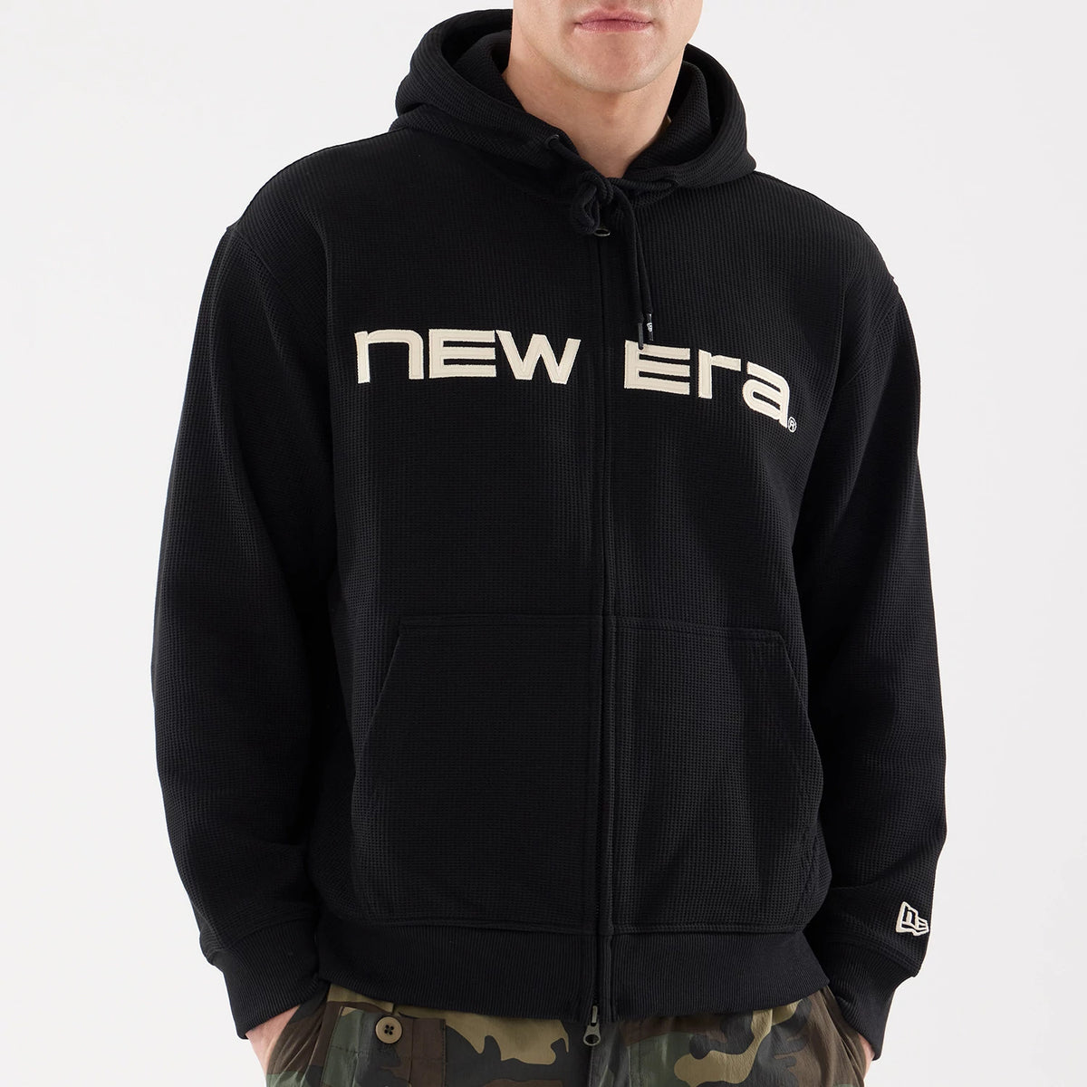 New Era Waffle Black Full Zip Hoodie, front view showing the black textured fabric with a raised New Era logo across the chest, the full zip running down the centre, and an embroidered New Era logo on the left sleeve cuff.