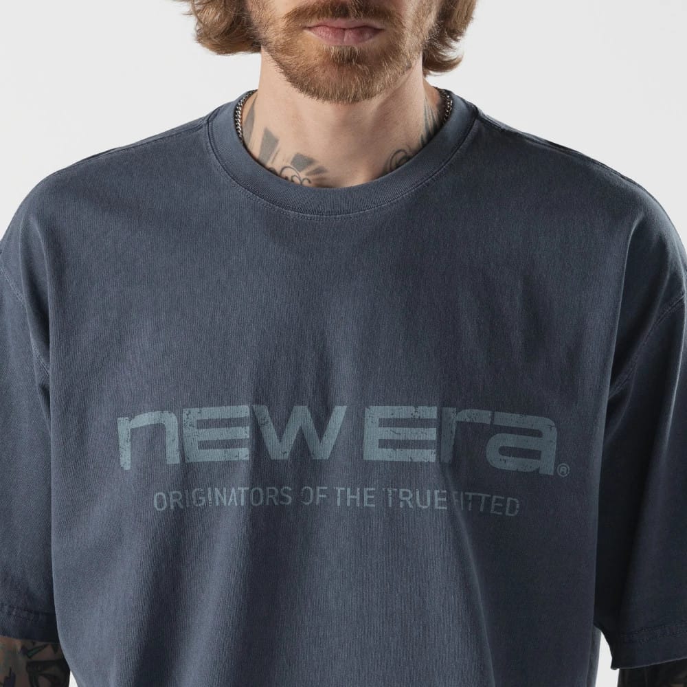 New Era Originators Navy T-Shirt, front view showing the navy fabric with a large debossed New Era logo across the chest, text reading "ORIGINATORS OF THE TRUE FITTED" below the logo, and a classic crew neckline.