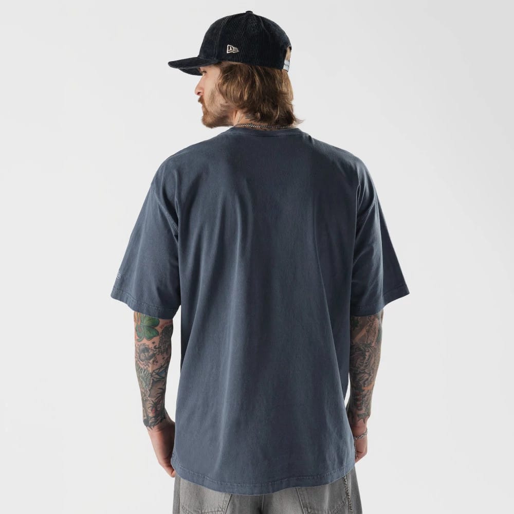 New Era Originators Navy T-Shirt, on-model view showing the back of the navy T-shirt worn by a person with tattoos on their arms, paired with a black cap featuring an embossed New Era logo on the side.