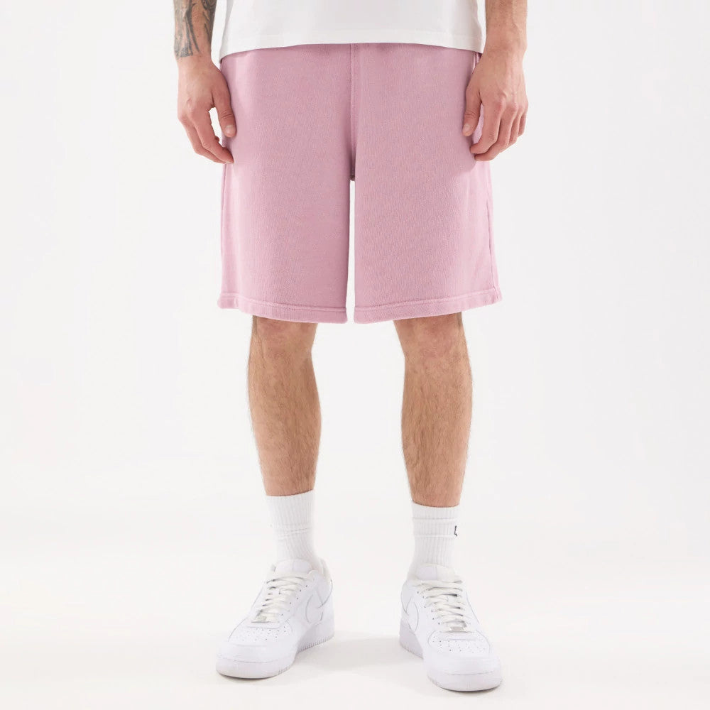 New Era Originators Pink Oversized Shorts, front view showing the light pink colour extending to just below the knee, with a loose fit design and a plain hem, worn with white socks and trainers.