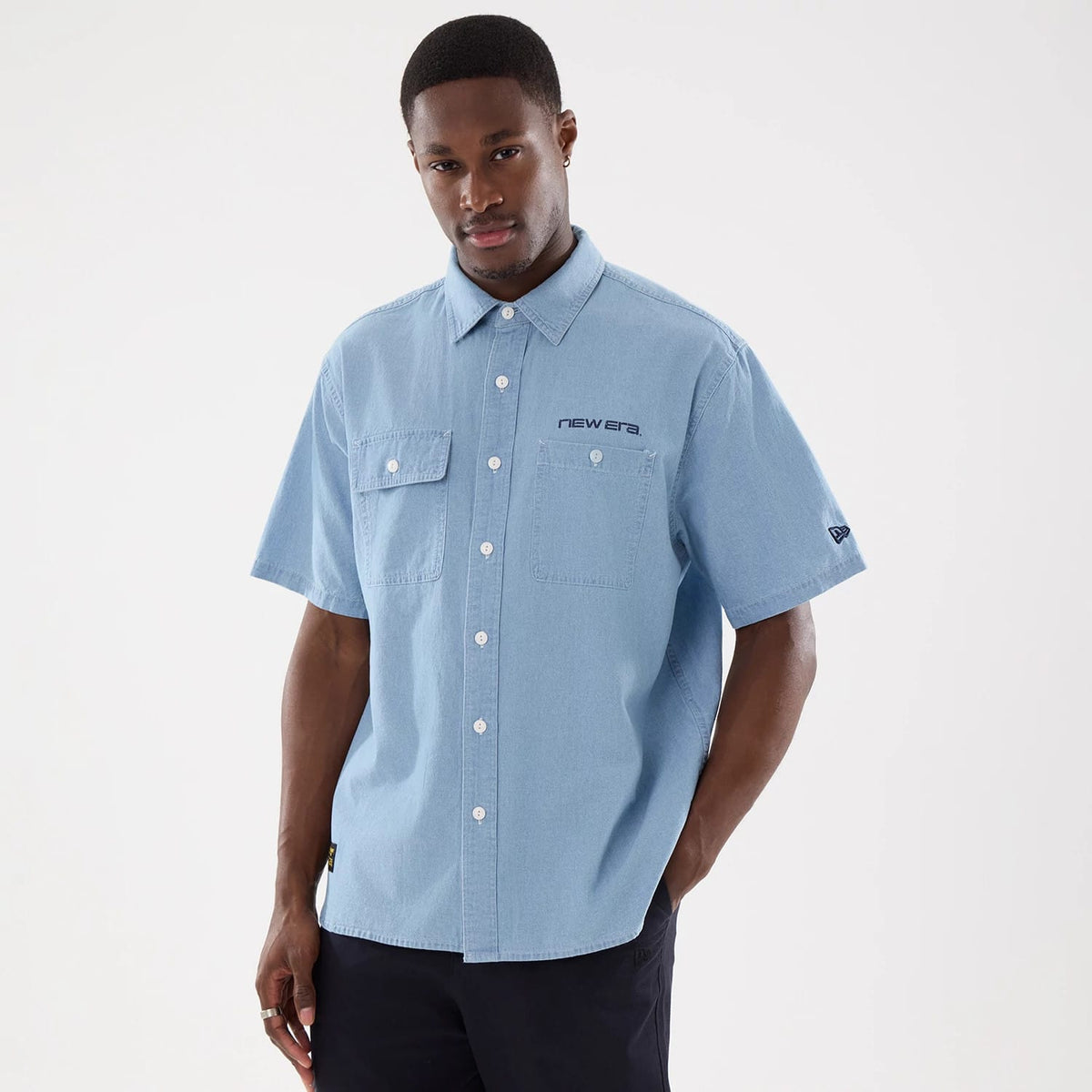 New Era Originators Chambray Bright Blue Short Sleeve Shirt, front view on a model with button-down design, two chest pockets, embroidered New Era text on the left chest, and the New Era flag logo on the left sleeve.