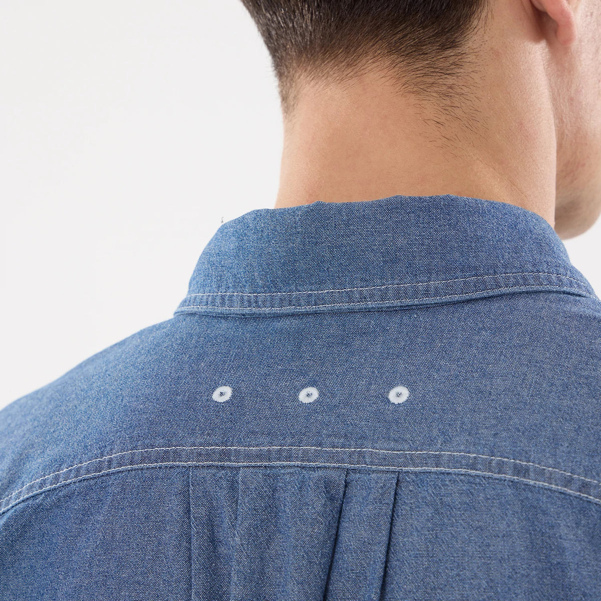 New Era Originators Chambray Dark Blue Short Sleeve Shirt, rear view on a model showing detailed stitching and pleats at the back, with contrasting white embroidered eyelets below the collar.