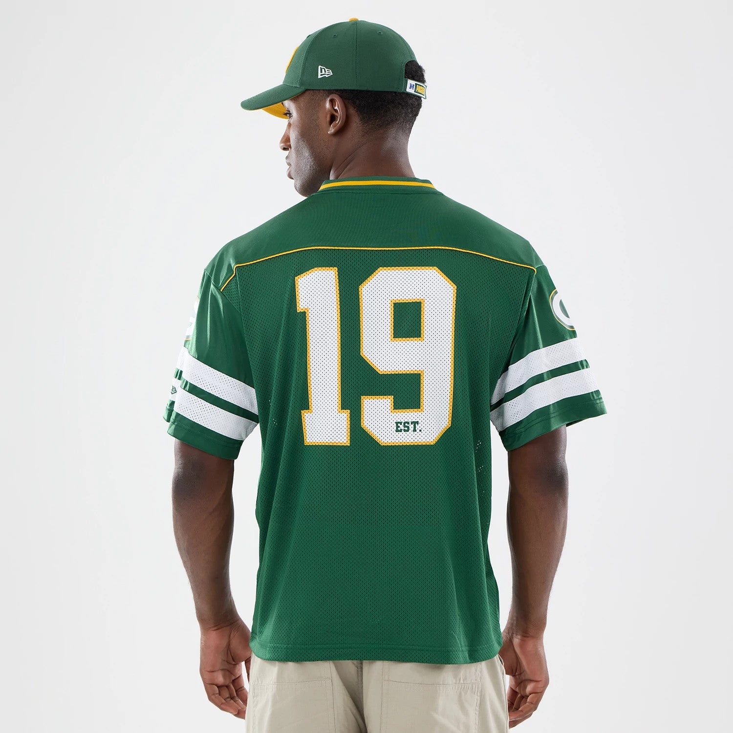 Green Bay Packers NFL Green Mesh Jersey, back view on a model with a matching cap, featuring white number 19 with EST. lettering, and double white stripes on the sleeves against a green mesh fabric.