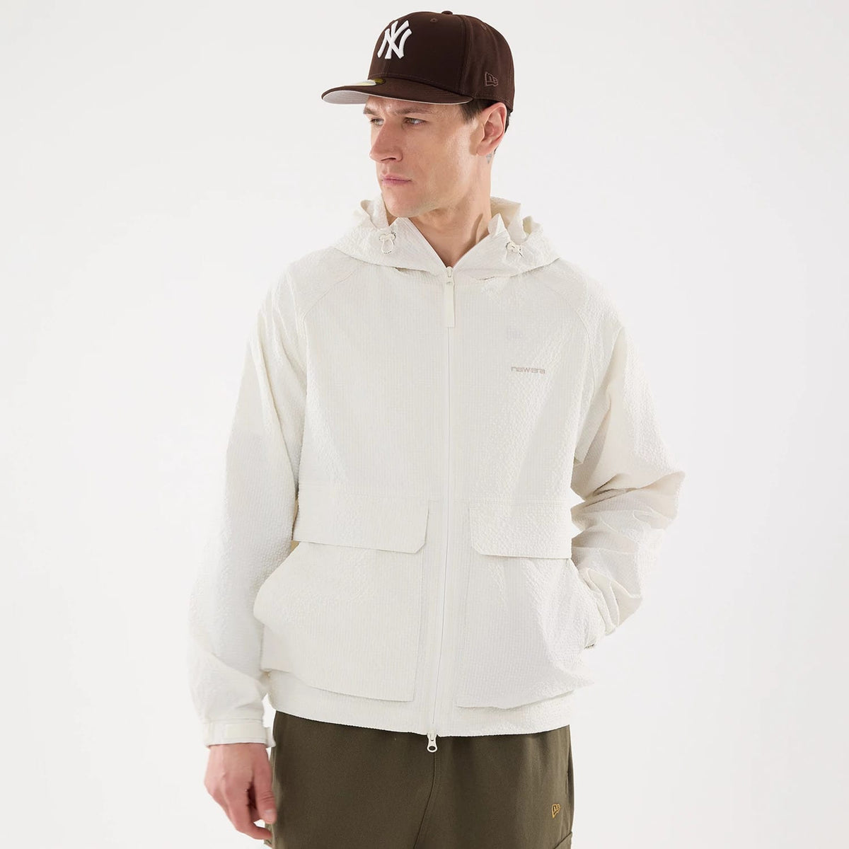 New Era Black Label Open White Jacket, on-model view showing a front zip closure, spacious front pockets, and a hood with drawstrings, worn by a person also wearing a brown cap with a white raised logo.