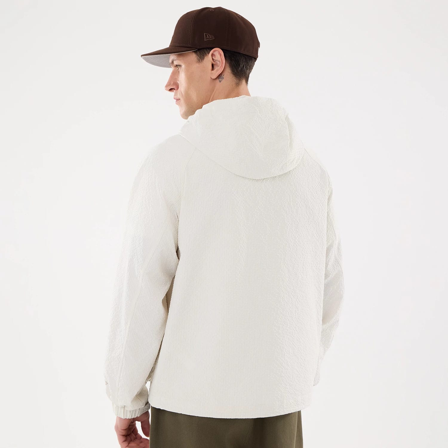 New Era Black Label Open White Jacket, on-model view showing the back of the white jacket with a hood and elastic cuffs, the model is wearing a brown cap with an embossed New Era logo on the side.