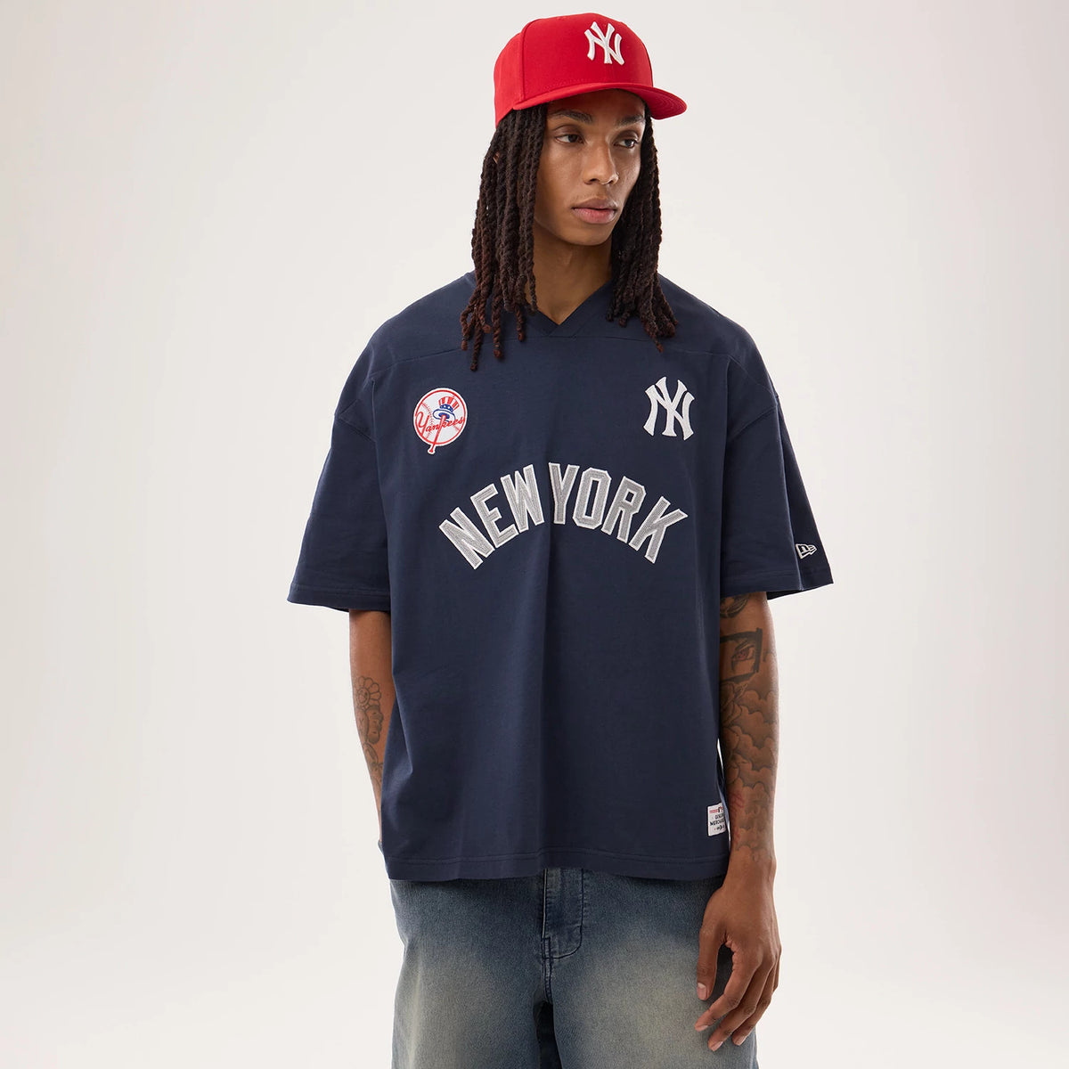 New York Yankees MLB Fan Family Navy Jersey, front view on a model wearing a red cap, featuring a Yankees logo on the left chest, a New York wordmark across the chest, and a Yankees patch on the right chest.
