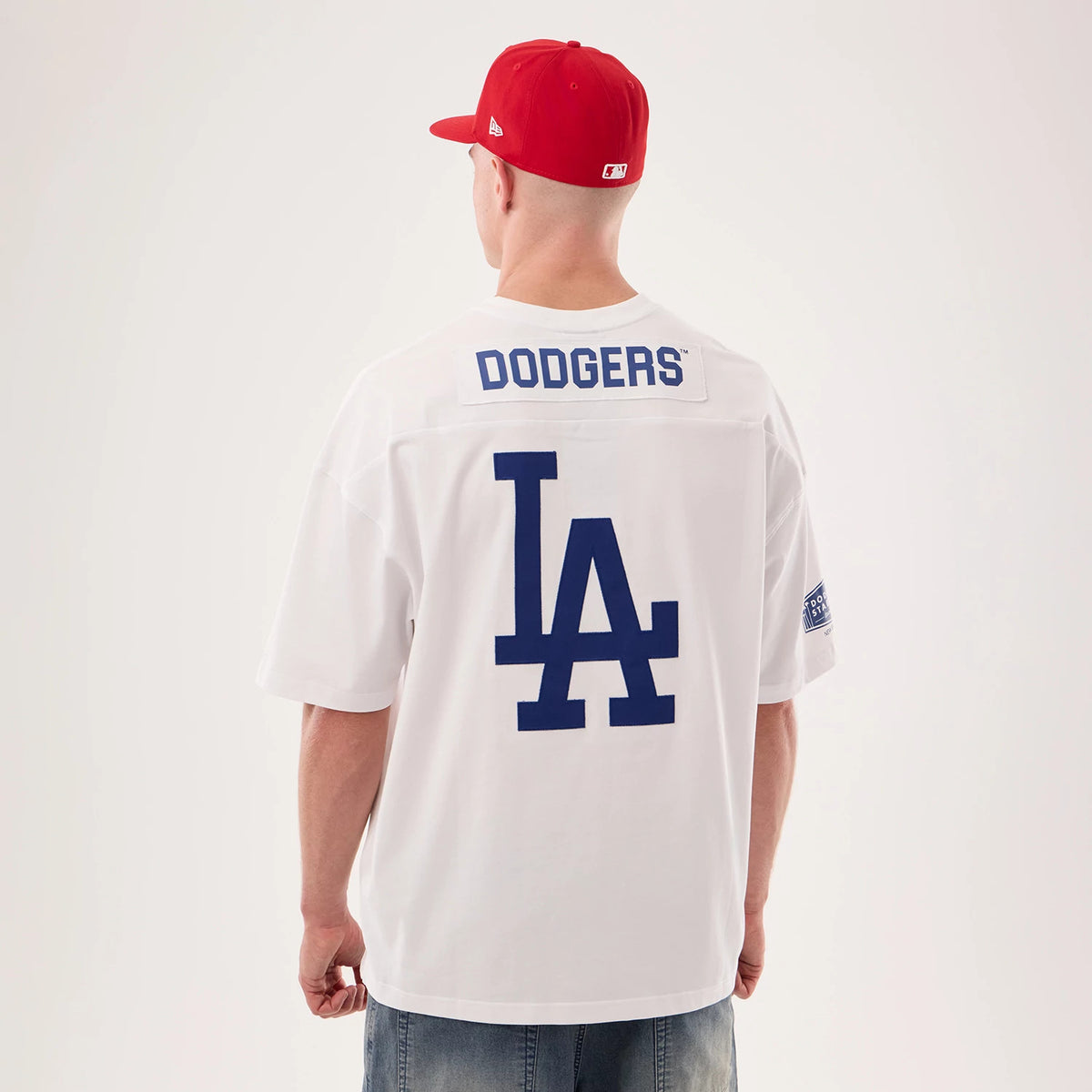 Los Angeles Dodgers MLB Fan Family White Jersey, back view on a model wearing a matching red cap, featuring blue DODGERS lettering above a large LA logo and sleeve patch detailing.