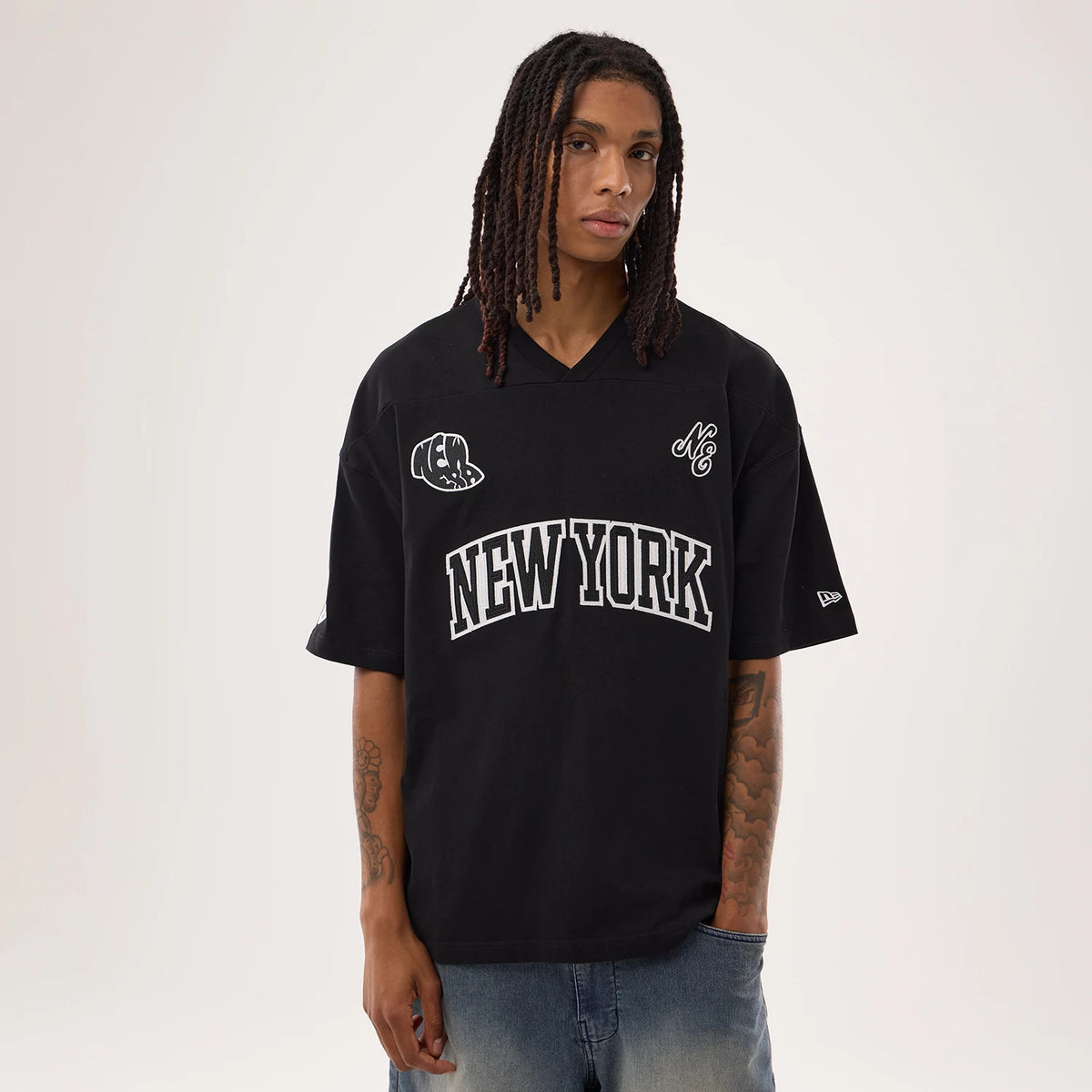 New Era Fan Family Black Jersey, front view on a model wearing jeans, featuring large white New York lettering across the chest, an embroidered bear logo on the right side, and the New Era flag logo on the left sleeve.
