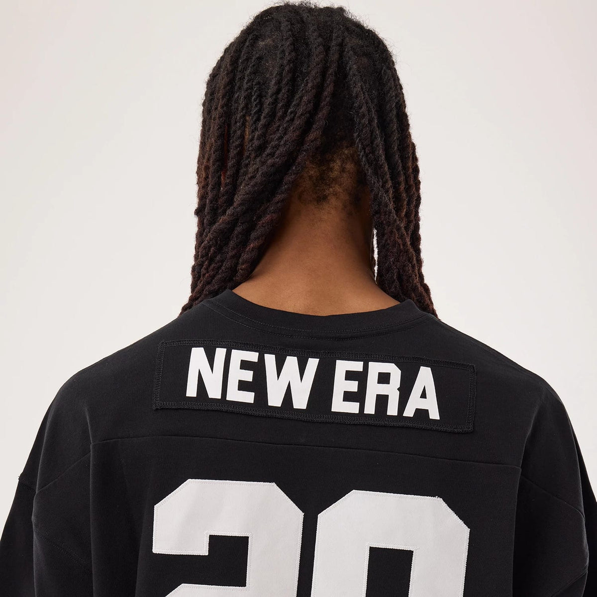 New Era Fan Family Black Jersey, back view on a model with long braided hair, featuring bold white "NEW ERA" lettering across the upper back and large number "20" in white below it on the black fabric.