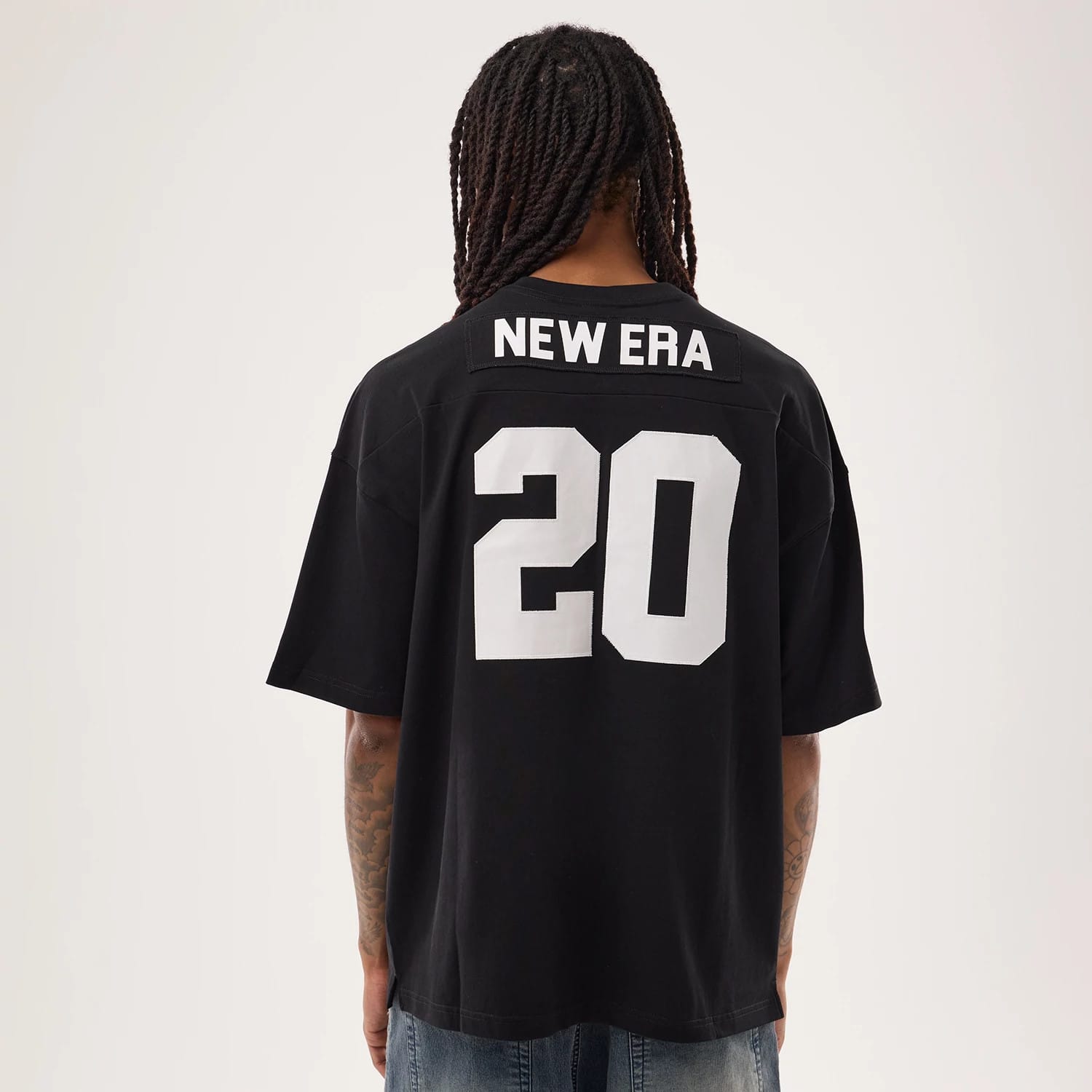 New Era Fan Family Black Jersey, back view on a model styled with denim jeans, featuring large white '20' numbering centred below 'NEW ERA' lettering across the shoulders on the black fabric.