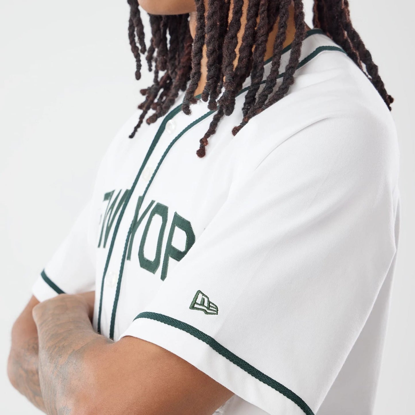 New Era New York White Jersey, three-quarter view on a model with dreadlocks, showing green piping along the button placket and sleeves, with an embroidered New Era flag logo on the left sleeve.
