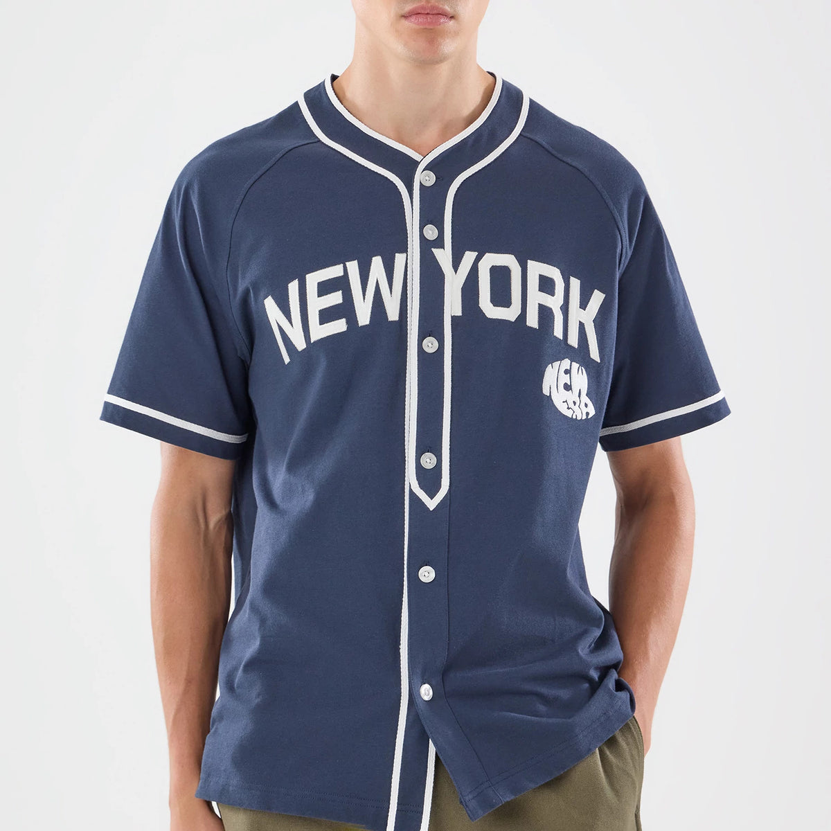 New Era New York Navy Jersey, front view on a model wearing khaki trousers, featuring white raglan sleeves with piping, button-up front with contrast trim, and an arched New York wordmark across the chest.