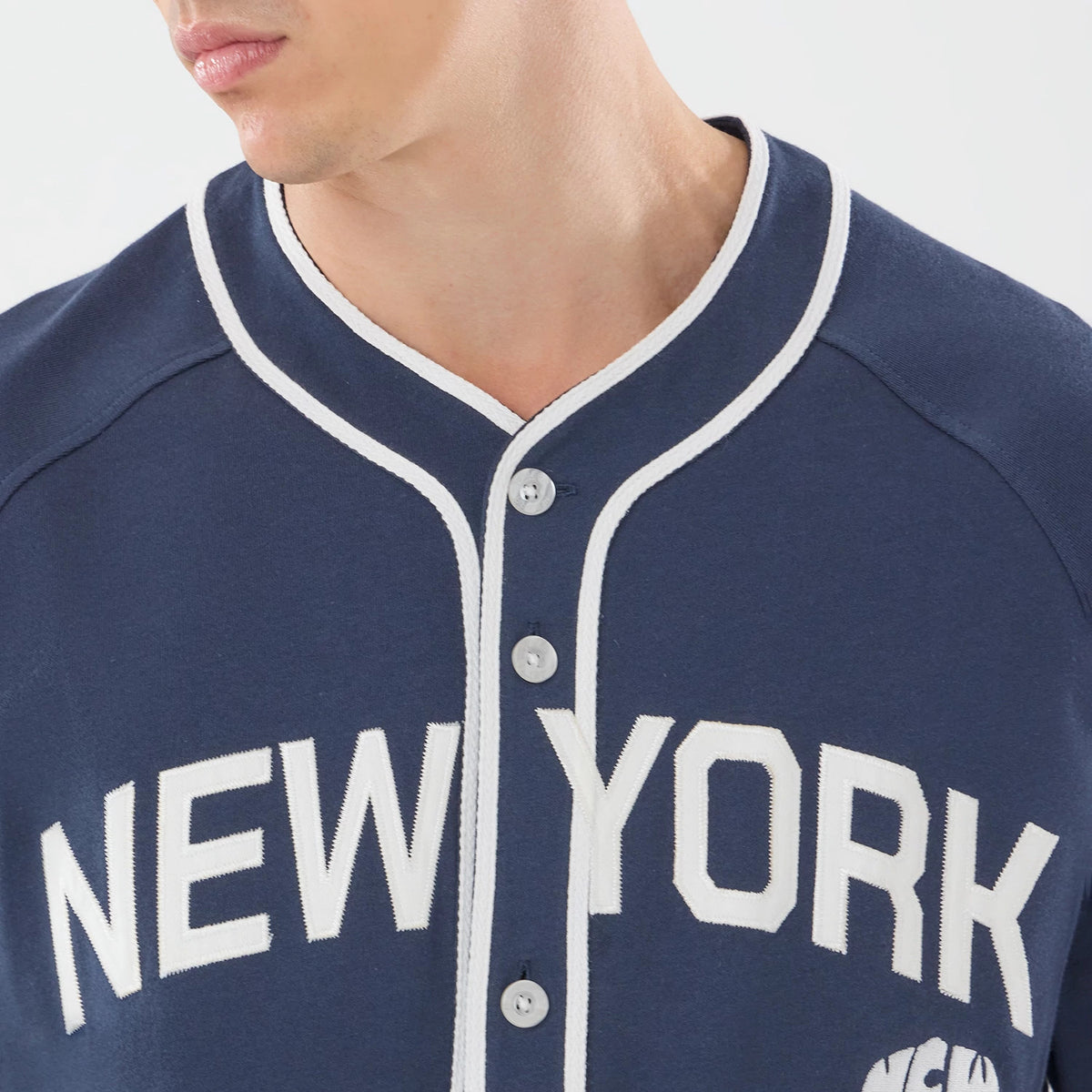 New Era New York Navy Jersey, three-quarter view on a model showing the front with white embroidered New York lettering, button-up design, and white trim along the collar and placket.