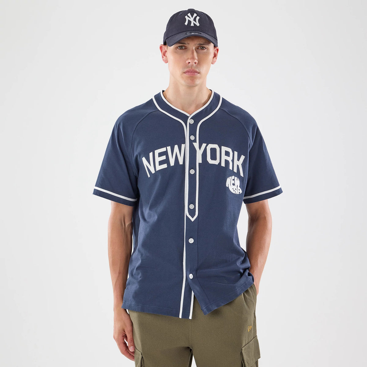 New Era New York Navy Jersey, front view on a model wearing a matching navy cap, featuring the New York wordmark in white across the chest and a New Era flag logo on the left sleeve.