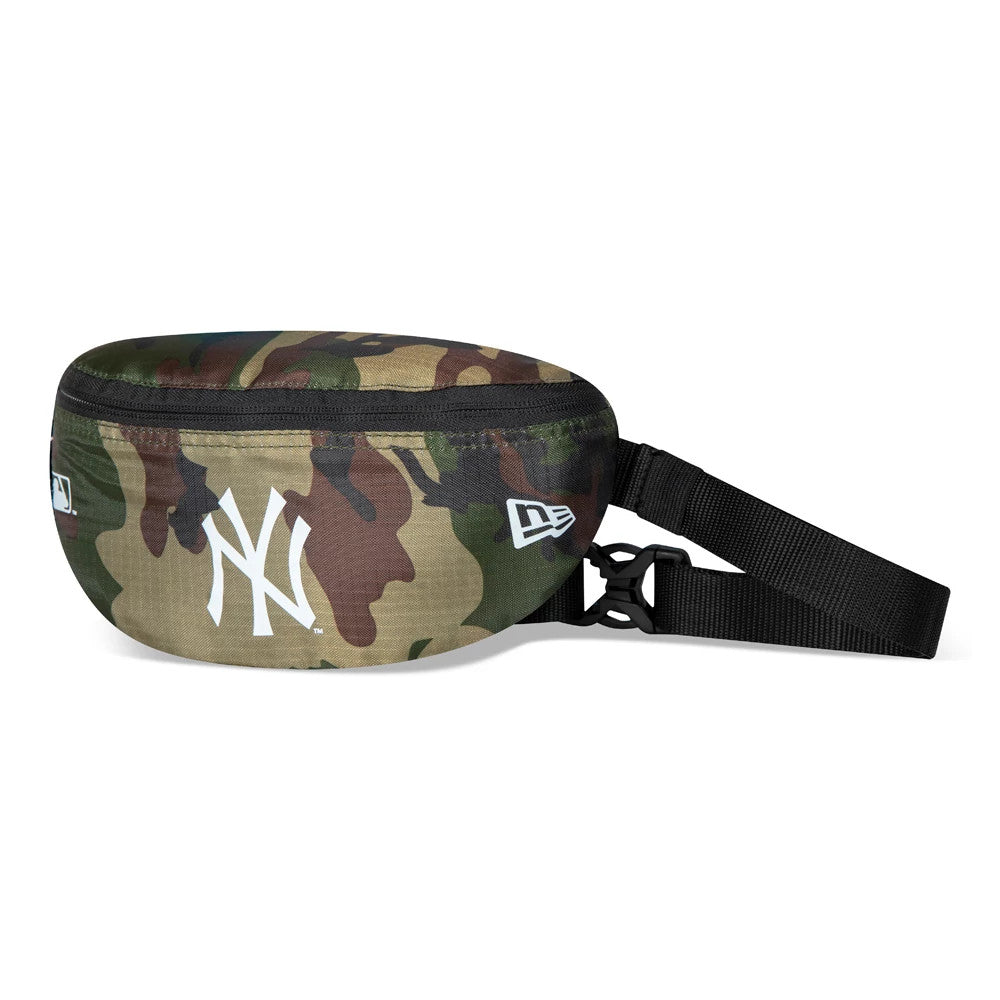 New York Yankees Camo Mini Waist Bag, side view displaying the camo-patterned exterior with a black adjustable strap, a zip closure along the top, and a raised white New Era logo next to a large white Yankees emblem on the front.