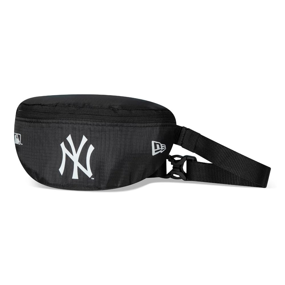 New York Yankees Black Mini Waist Bag, side view showing the sleek black design with a raised New York Yankees logo in white on the front, a zip running along the top and an adjustable black strap with a buckle on the side.