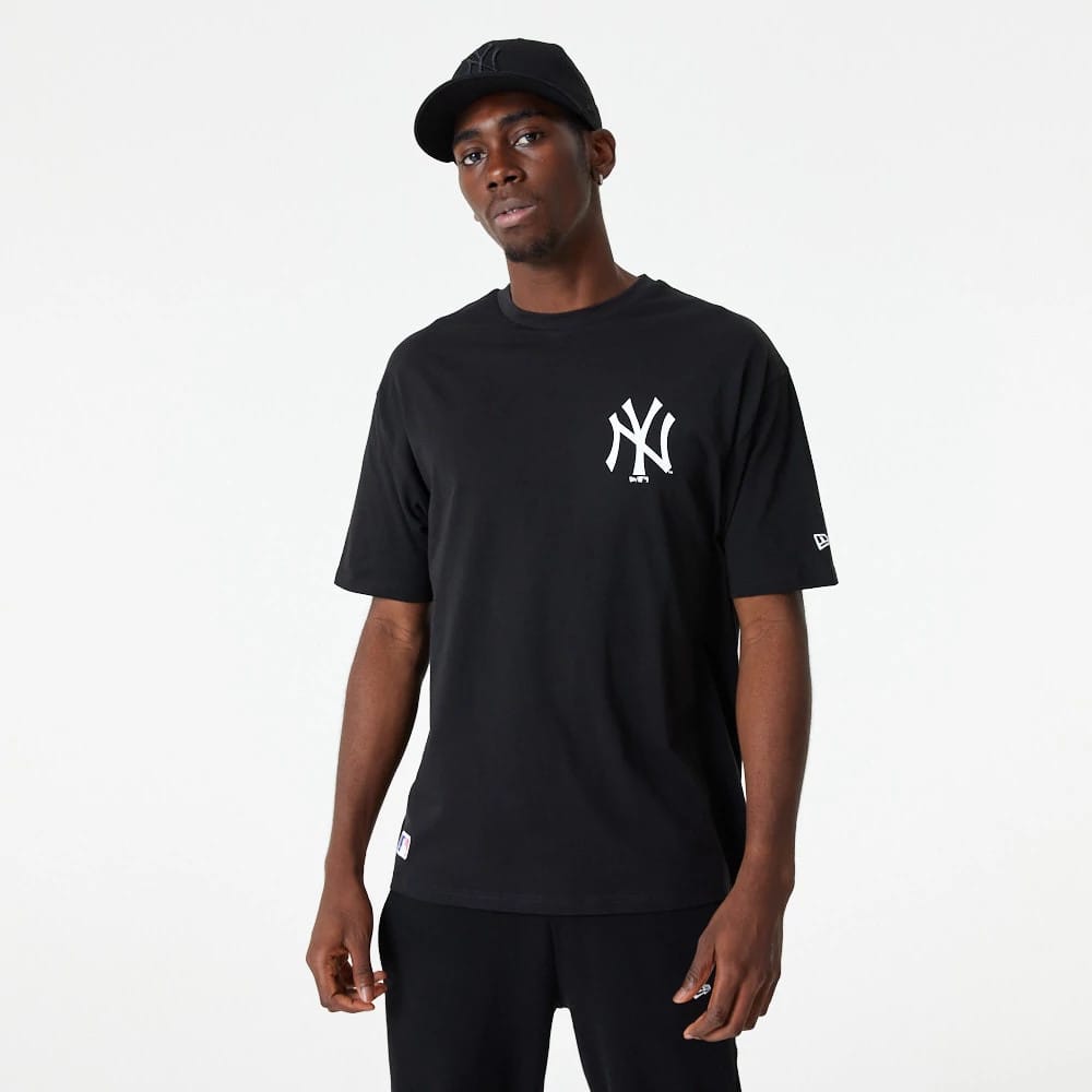 New York Yankees MLB Essential Black Oversized T-Shirt, on-model front view showing a large white NY logo on the left chest and a small white New Era logo on the left sleeve, paired with a black cap also featuring an embroidered NY logo.