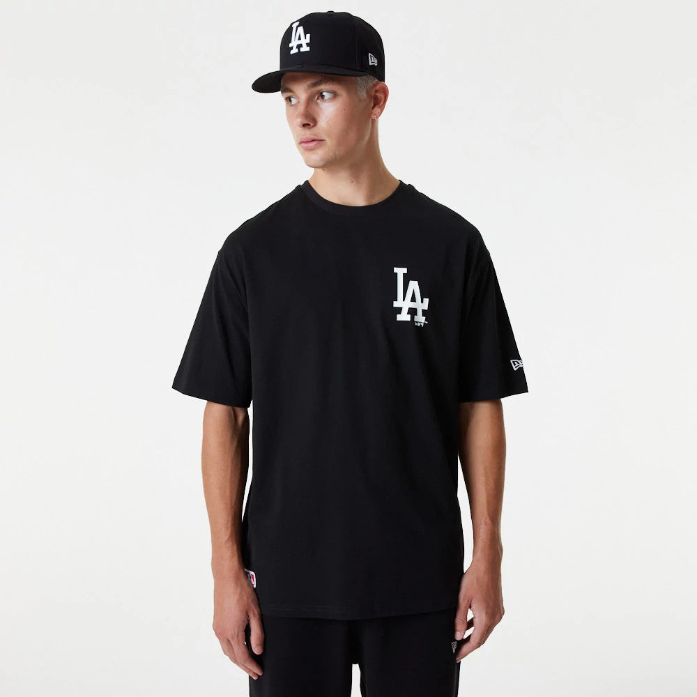 LA Dodgers MLB Essential Black Oversized T-Shirt, on-model view showing the black oversized fit with a white LA logo printed on the left chest, paired with a black cap also featuring the white LA logo, by New Era.