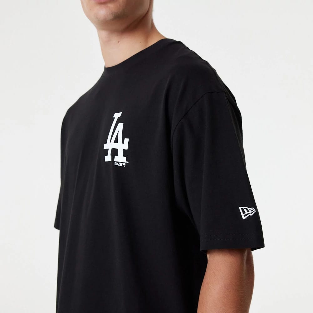 LA Dodgers MLB Essential Black Oversized T-Shirt, side view showing the bold white LA logo printed on the left chest and a raised New Era logo on the left sleeve, both on the smooth black fabric.