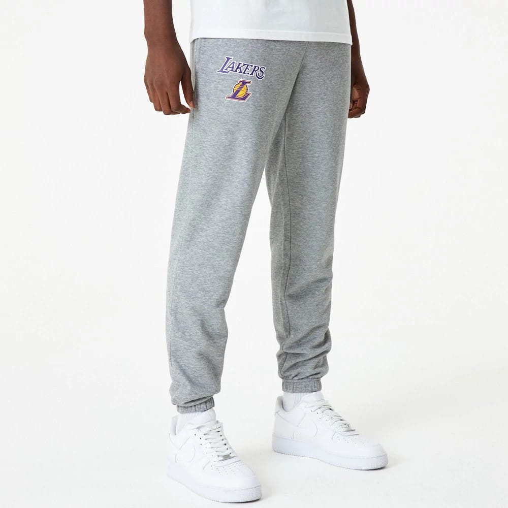 LA Lakers NBA Essential Grey Joggers, front view on a model showing the embroidered Lakers logo in purple and gold on the left thigh, with elasticated cuffs and relaxed fit, paired with white trainers.