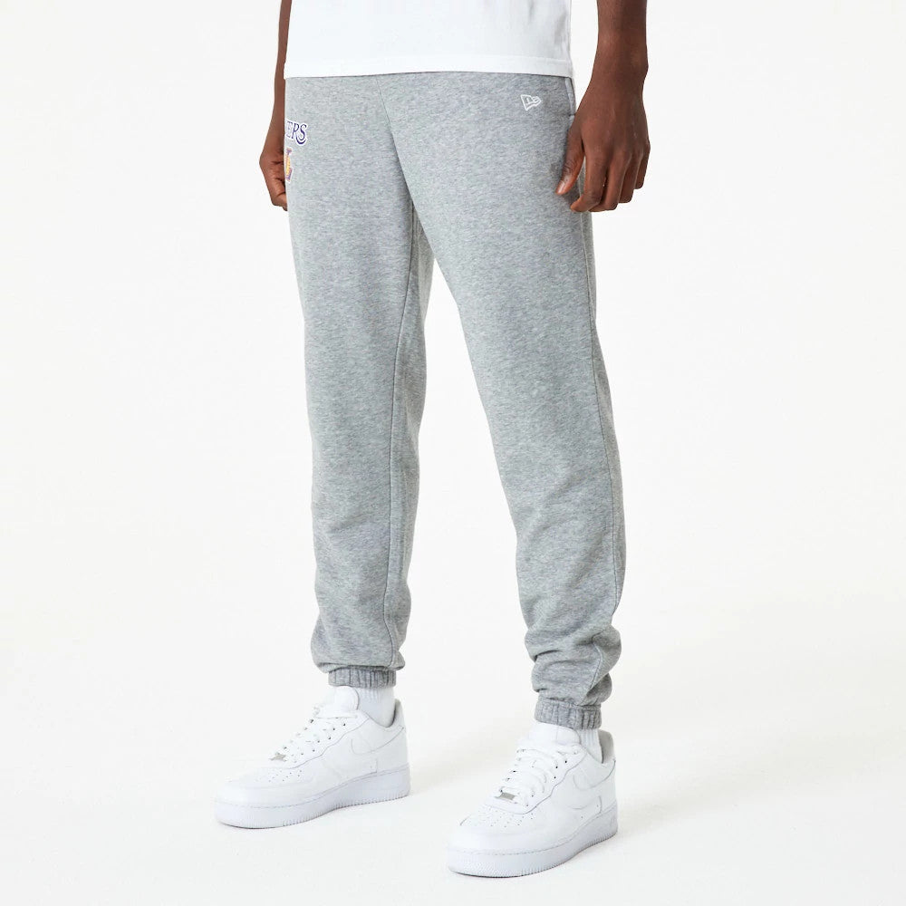 LA Lakers NBA Essential Grey Joggers, front view on a model wearing white trainers and a white shirt, showing the LA Lakers logo embroidered on the right leg and the New Era flag logo on the left pocket.