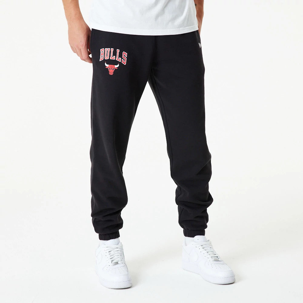 Chicago Bulls NBA Essential Black Joggers, front view on a model showing the red and white Bulls logo with the team's name on the left thigh, paired with a plain white T-shirt and white sneakers.