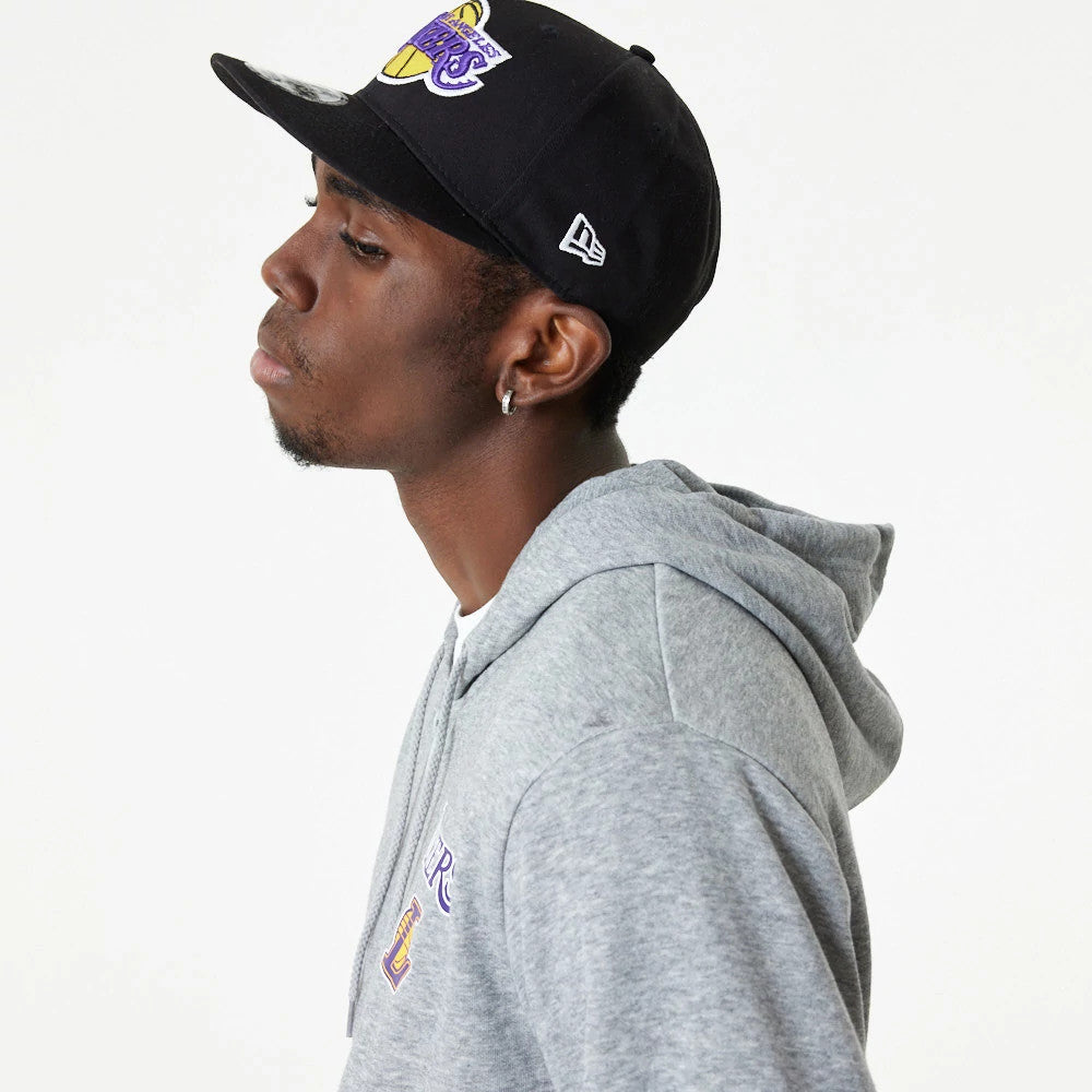 LA Lakers NBA Essential Grey Full Zip Hoodie, side view showing a grey hoodie with the Lakers logo on the chest, worn by a model, paired with a black cap featuring an embroidered logo on the side.