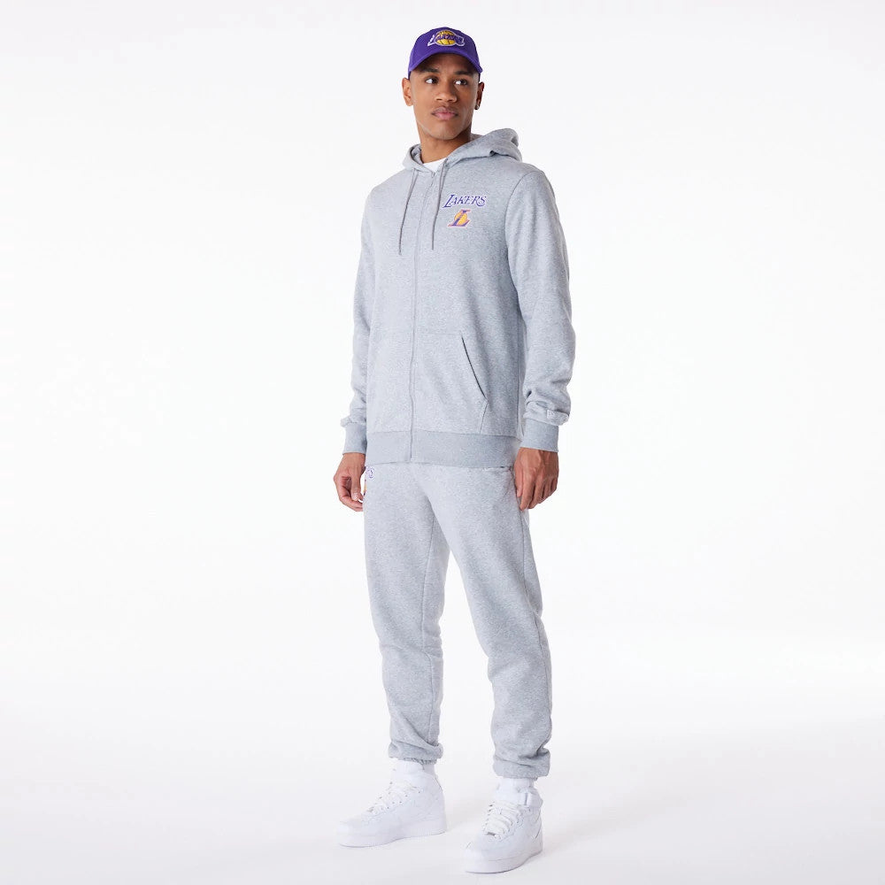 LA Lakers NBA Essential Grey Full Zip Hoodie, on-model view showing the light grey hoodie with an embroidered Lakers logo on the left chest, full-length zip, drawstring hood and ribbed cuffs, worn with matching sweatpants and white trainers.