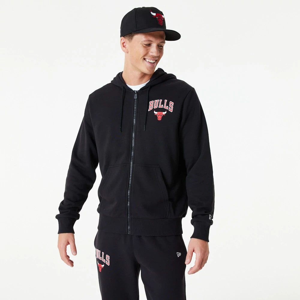 Chicago Bulls NBA Essential Black Full Zip Hoodie, on-model view showing a black hoodie with a full zip closure, Bulls logo on the left chest, and a black cap with an embroidered red Bulls logo worn by the model.