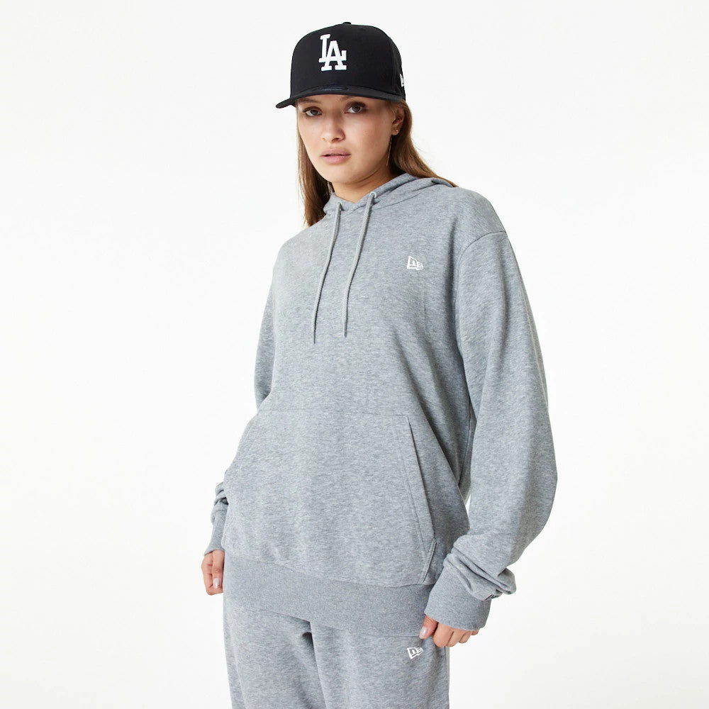 New Era Essential Grey Pullover Hoodie, on-model view showing a light grey hoodie with a raised New Era logo on the left chest, a large front pocket, and ribbed cuffs and hem, paired with a black cap featuring a raised white "LA" logo.