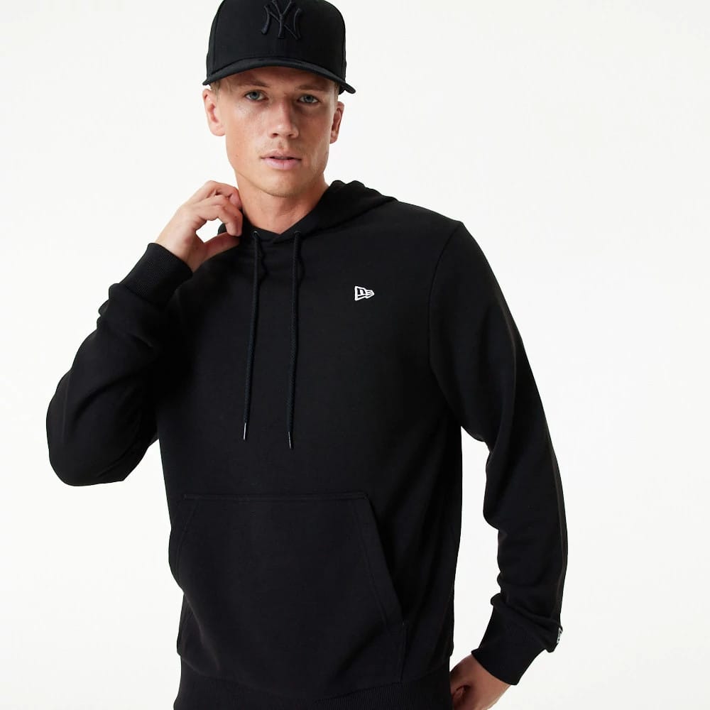 New Era Essential Black Pullover Hoodie, on-model view featuring a black hoodie with a small raised New Era logo on the left chest, long sleeves, ribbed cuffs, and a front pocket, paired with a black cap displaying a raised logo.