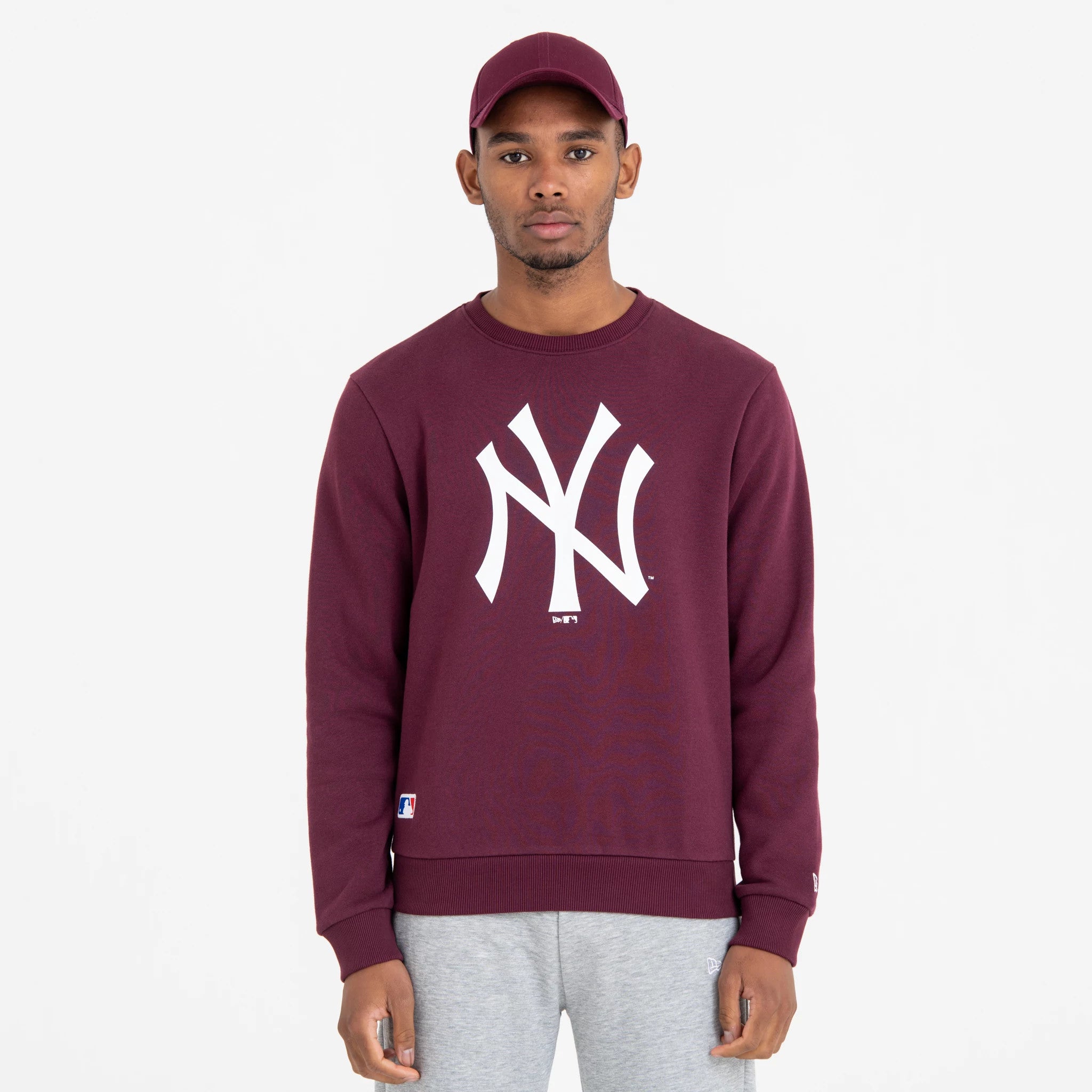 New York Yankees MLB Regular Dark Purple Crew Neck Sweatshirt, front view on a model wearing a matching cap, featuring a white NY logo centred on the chest and an MLB logo near the hem.