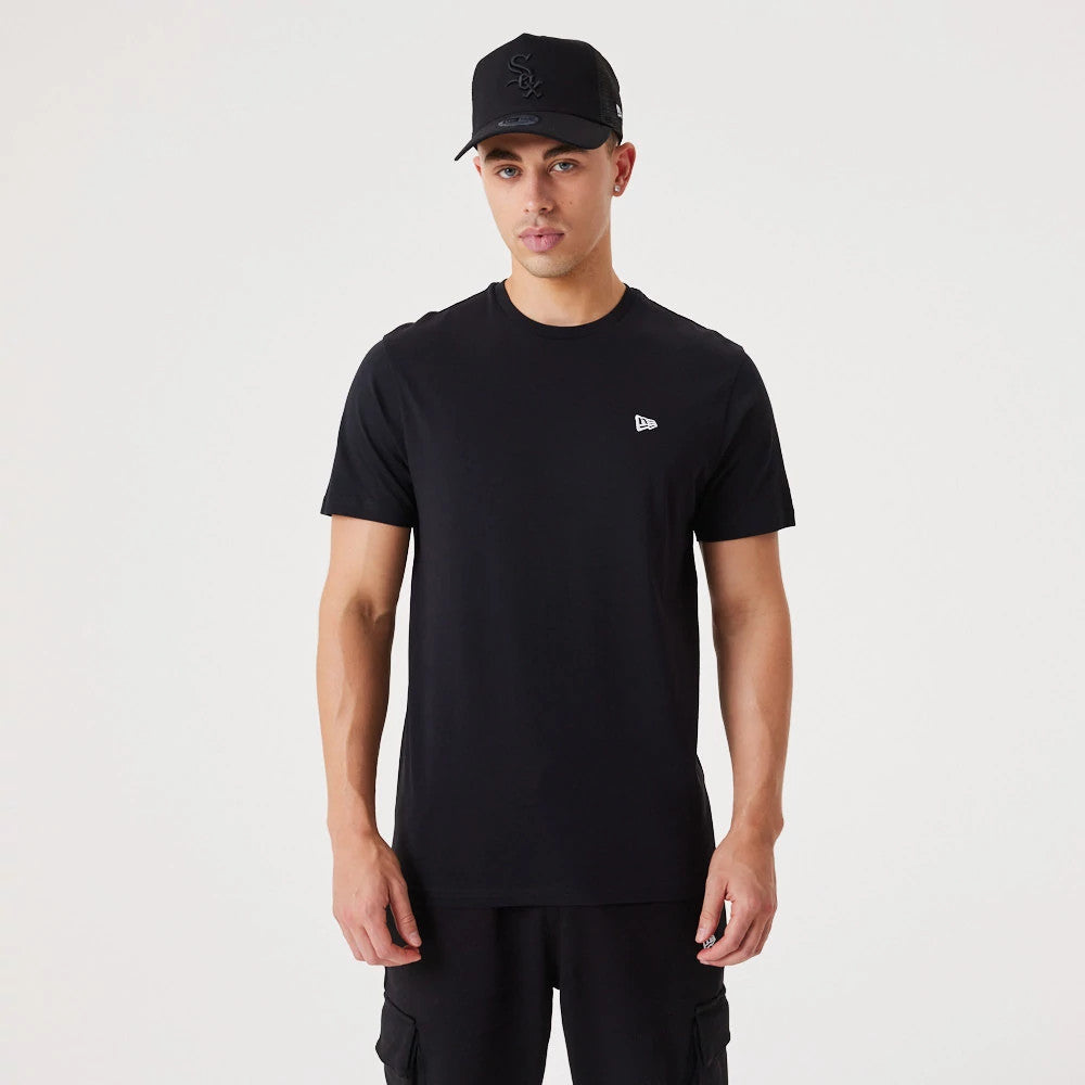 New Era Essential Black T-Shirt, front view showing a plain black t-shirt with a small white embroidered New Era logo on the left chest, worn by a model, paired with matching black shorts and a black cap with an embossed logo.