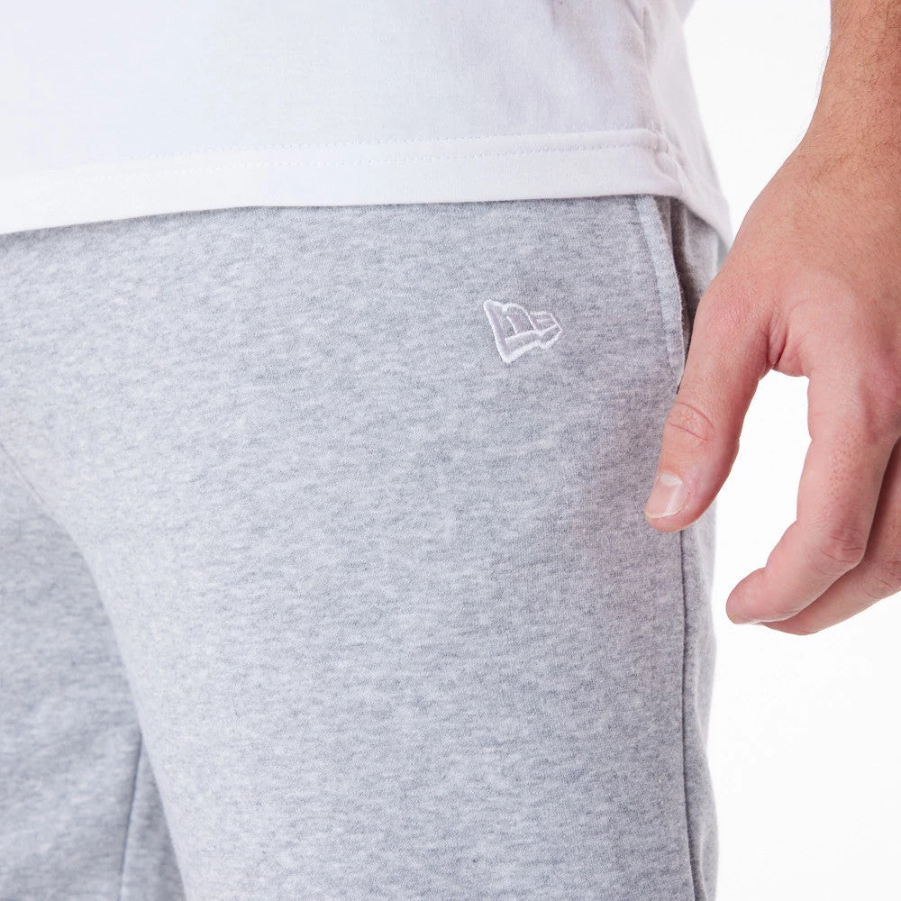 New Era Essential Grey Joggers, side view showing the New Era flag logo embroidered on the upper thigh, styled with a relaxed white T-shirt and focused on the soft jersey fabric texture.
