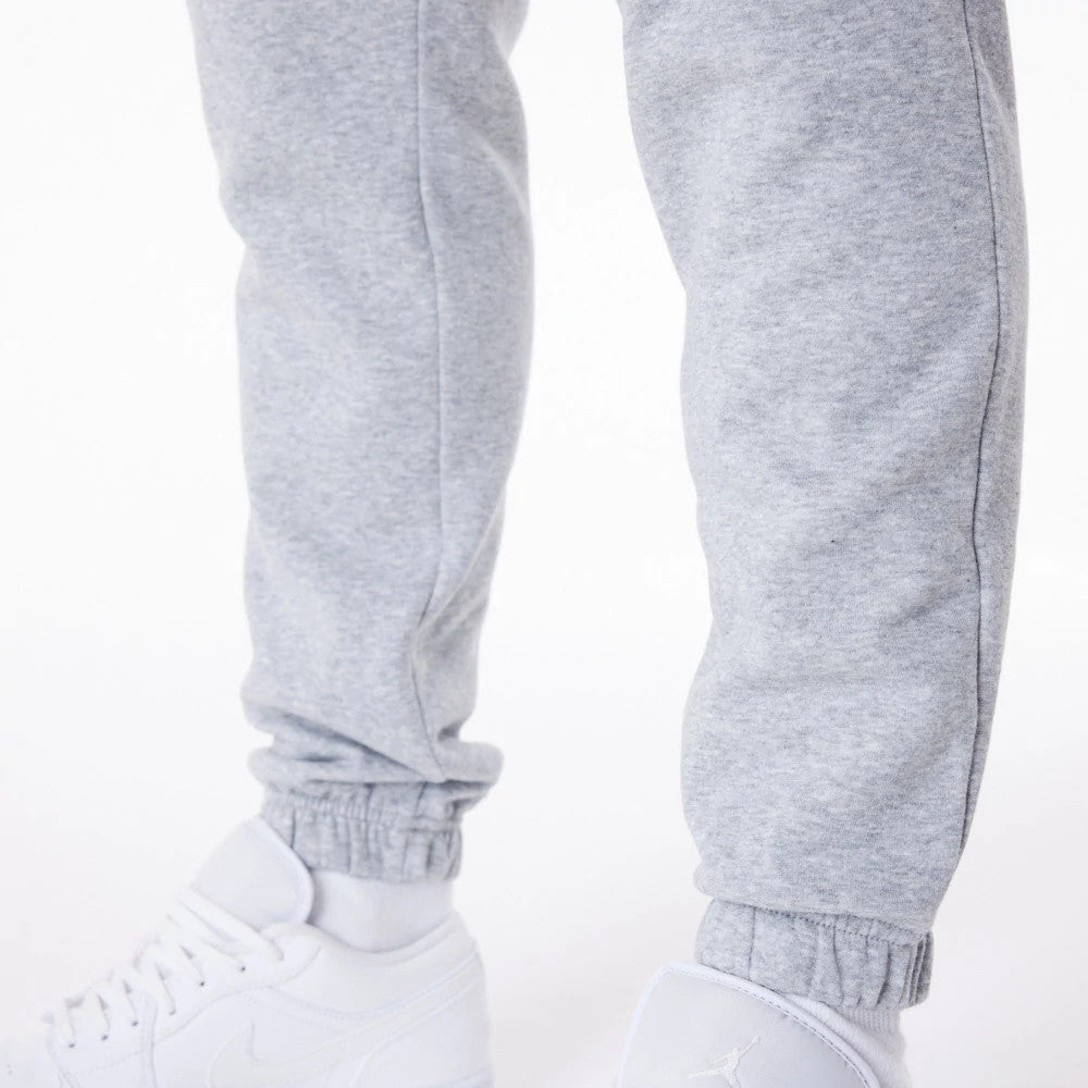 New Era Essential Grey Joggers, close-up view showing the elasticated cuffs at the ankles paired with white trainers, highlighting the soft grey fabric and casual fit.