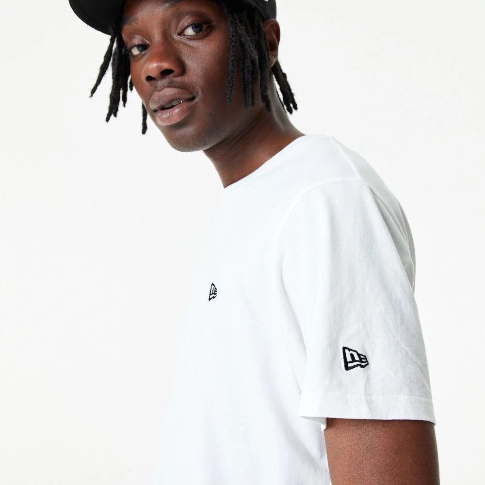 New Era Essential White T-Shirt, side view showing a clean white fabric with a small black embroidered New Era logo on the chest and another on the sleeve, worn by a model facing forward.