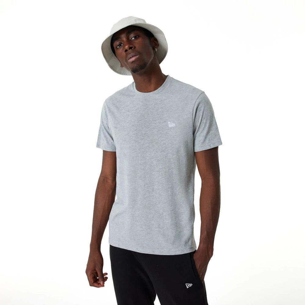 New Era Essential Grey T-Shirt, on-model view showing the light grey short-sleeved shirt with a small raised logo on the left chest, paired with black trousers featuring a similar logo, worn with a white bucket hat.