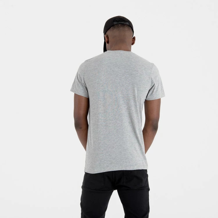 Milwaukee Bucks NBA Regular Grey T-Shirt, rear view showing the straight hem of the grey t-shirt, worn by a person standing with hands clasped behind the back, paired with black trousers and a backwards black cap.