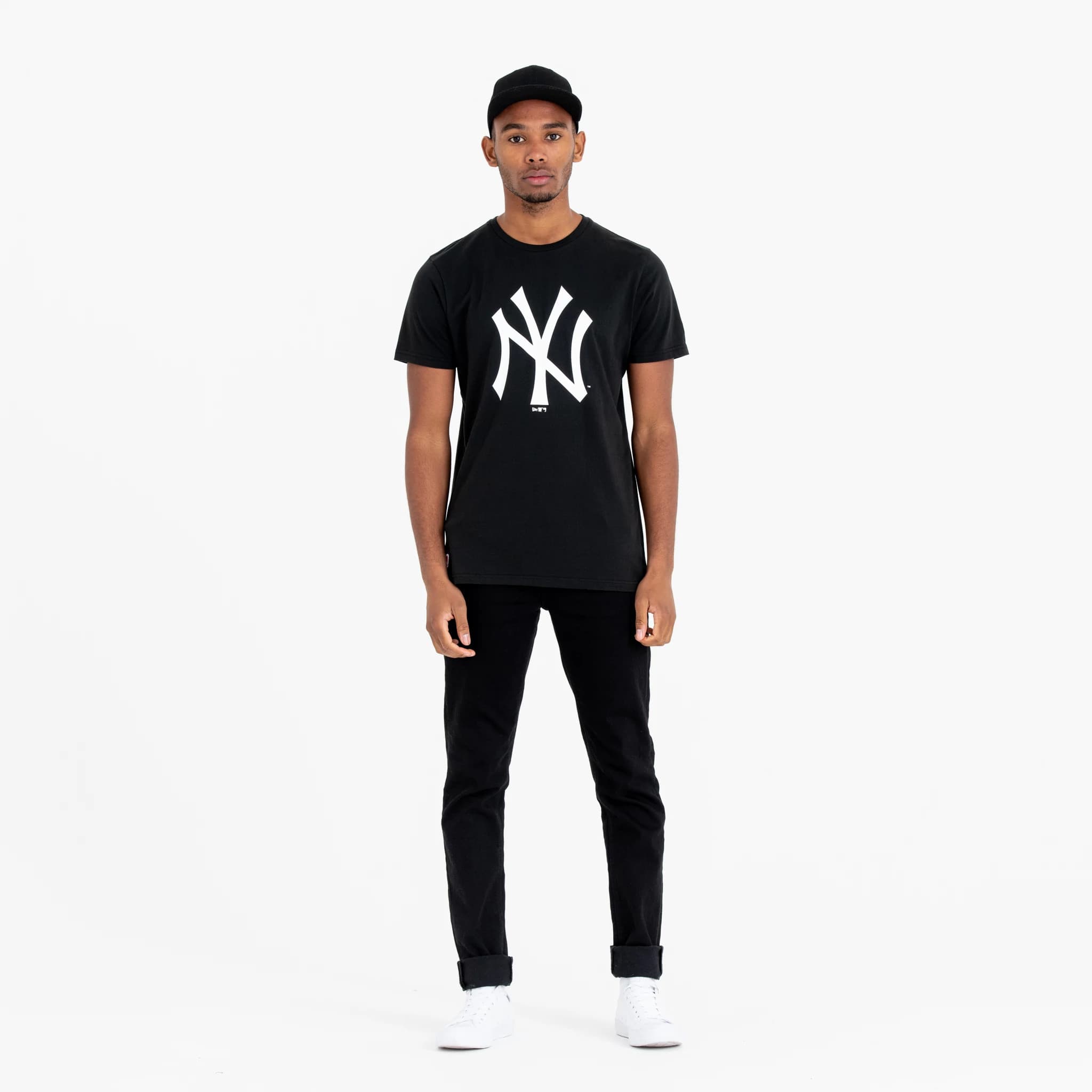 New York Yankees MLB Regular Black T-Shirt, on-model front view showing the bold white NY logo printed large on the chest of the black T-shirt, paired with black jeans and a black cap.