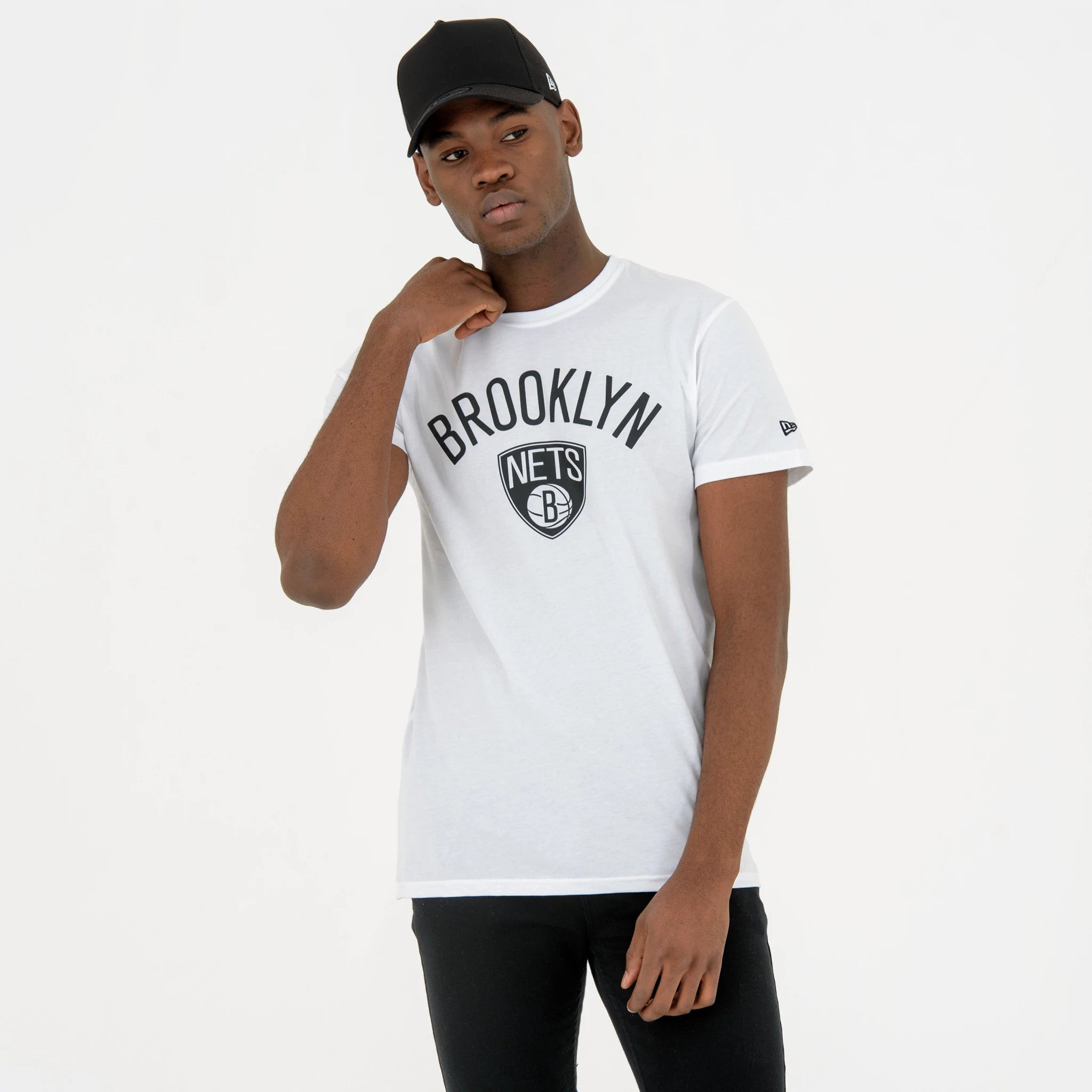 Brooklyn Nets NBA Regular White T-Shirt, on-model view showing the black Brooklyn Nets logo and lettering on the white fabric, a small debossed New Era logo on the left sleeve, with a model wearing a black cap in the picture.